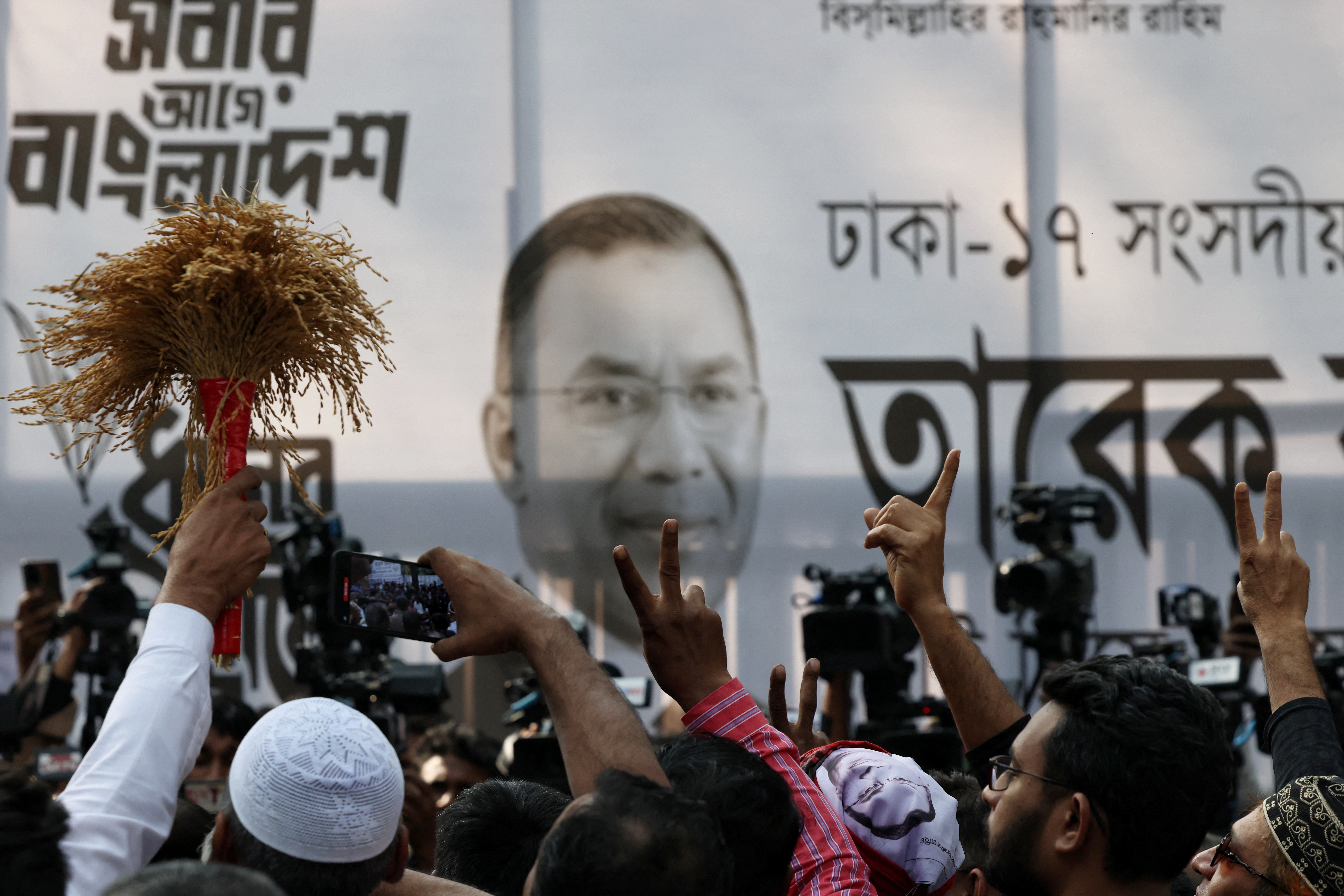 Supporters of the Bangladesh Nationalist Party (BNP) show a victory sign in front of a banner with Tarique Rahman’s photo, as the results project BNP's victory in the 13th general election, in Dhaka, Bangladesh, February 13, 2026