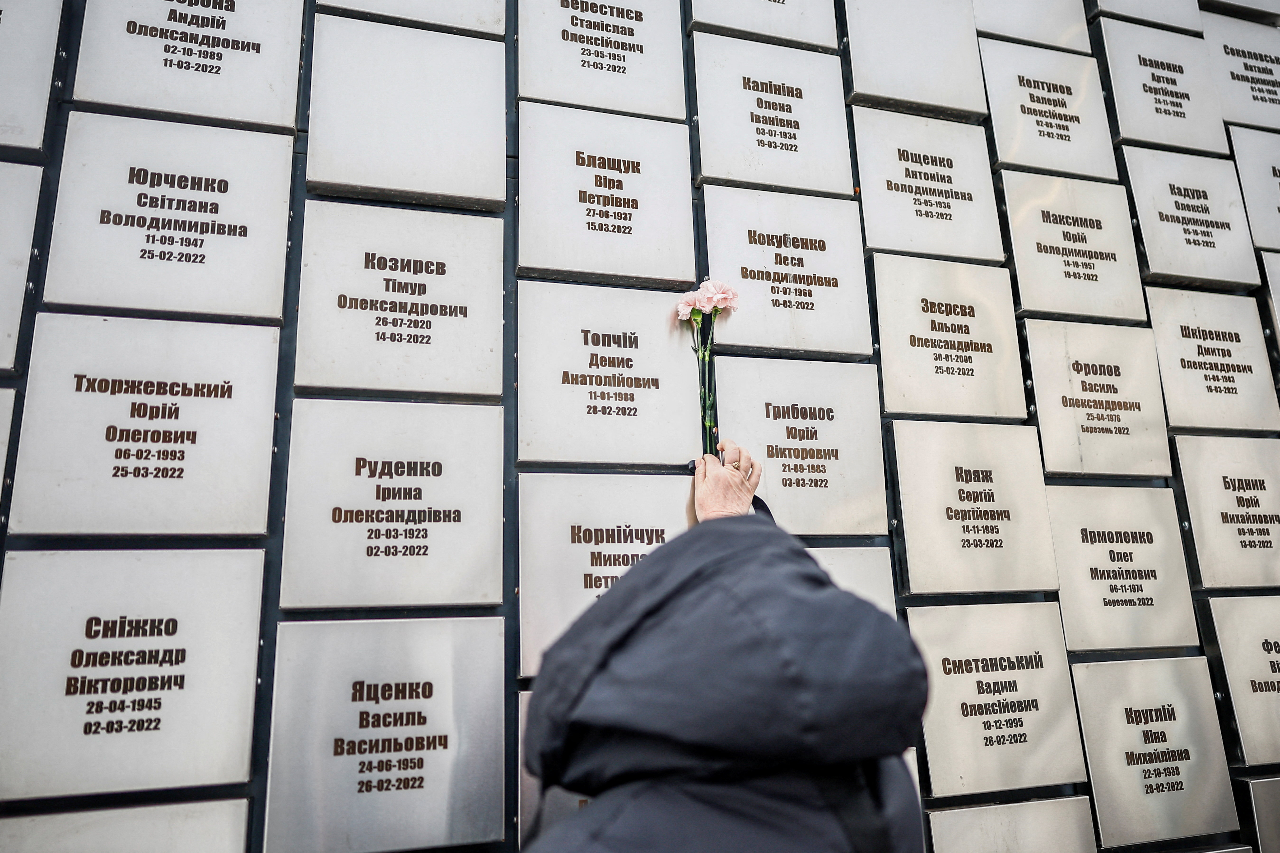 A woman brings flowers to pay tribute to the memorial installation for the victims of attacks and executions by Russian troops, marking the fourth anniversary of the full-scale Russian invasion, amid Russia's attack on Ukraine, in the town of Bucha, Kyiv region, Ukraine, February 24, 2026. REUTERS/Alina Smutko TPX IMAGES OF THE DAY