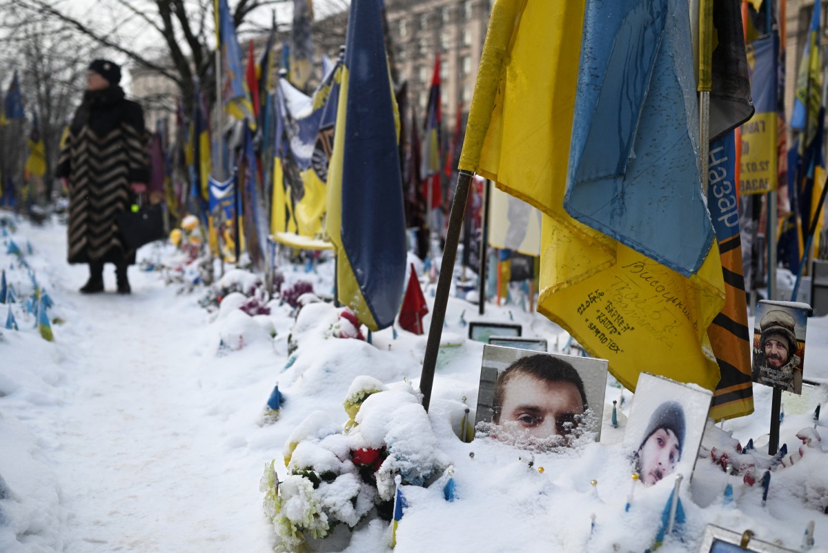 A woman visits the snow-covered memorial for the fallen Ukrainian and foreign fighters on Independence Square in Kyiv on January 13, 2026, amid the Russian invasion of Ukraine. (Photo by Sergei GAPON / AFP)