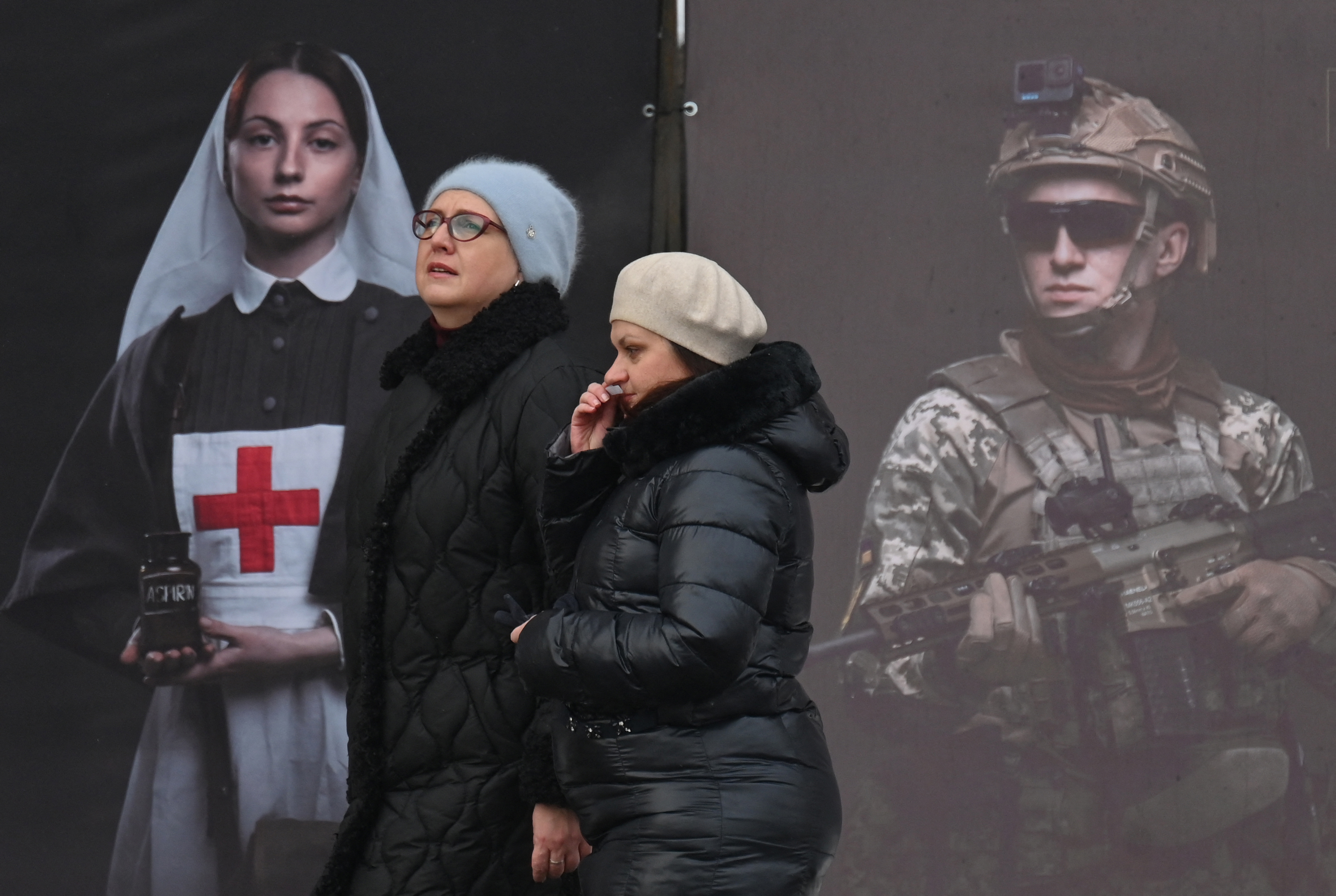 Women walk past a poster displayed by the National Institute of National Remembrance as part of an open air exhibition in the center of Kyiv on February 8, 2026, amid the Russian invasion in Ukraine. (Photo by Sergei SUPINSKY / AFP)