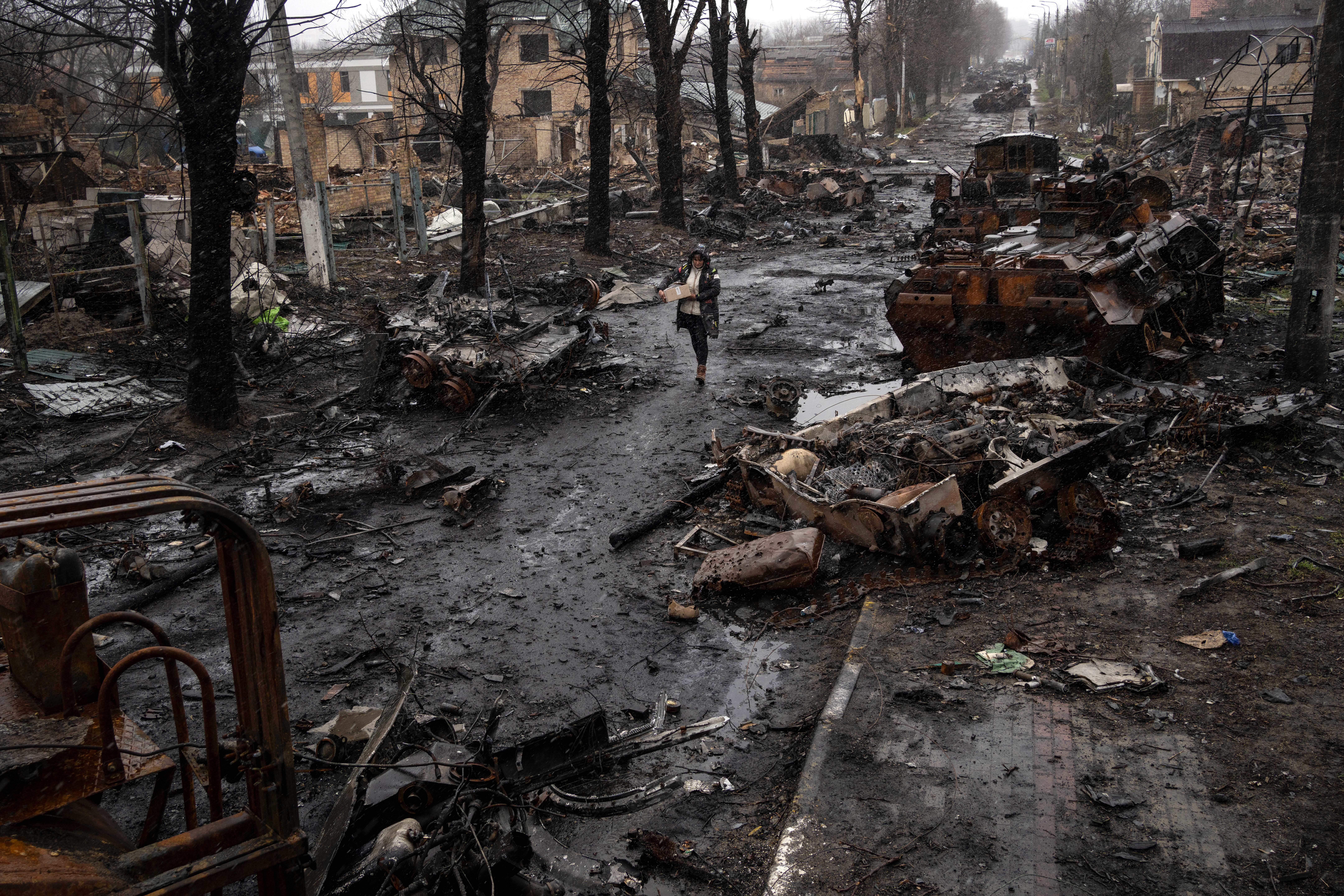 A woman navigates a debris-filled street where destroyed Russian military vehicles stand.