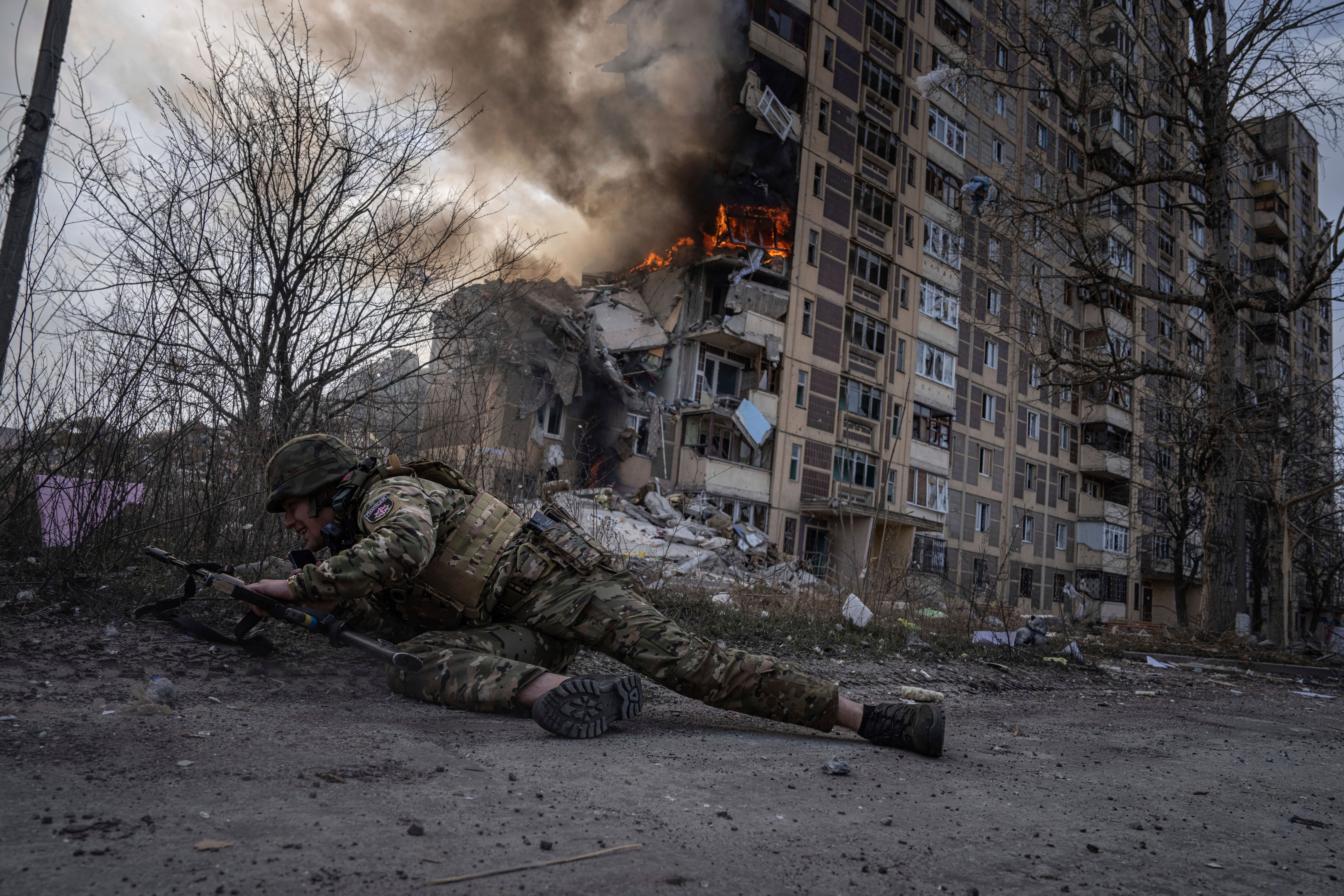 A Ukrainian police officer takes cover in front of a burning building that was hit in a Russian airstrike in Avdiivka, Ukraine