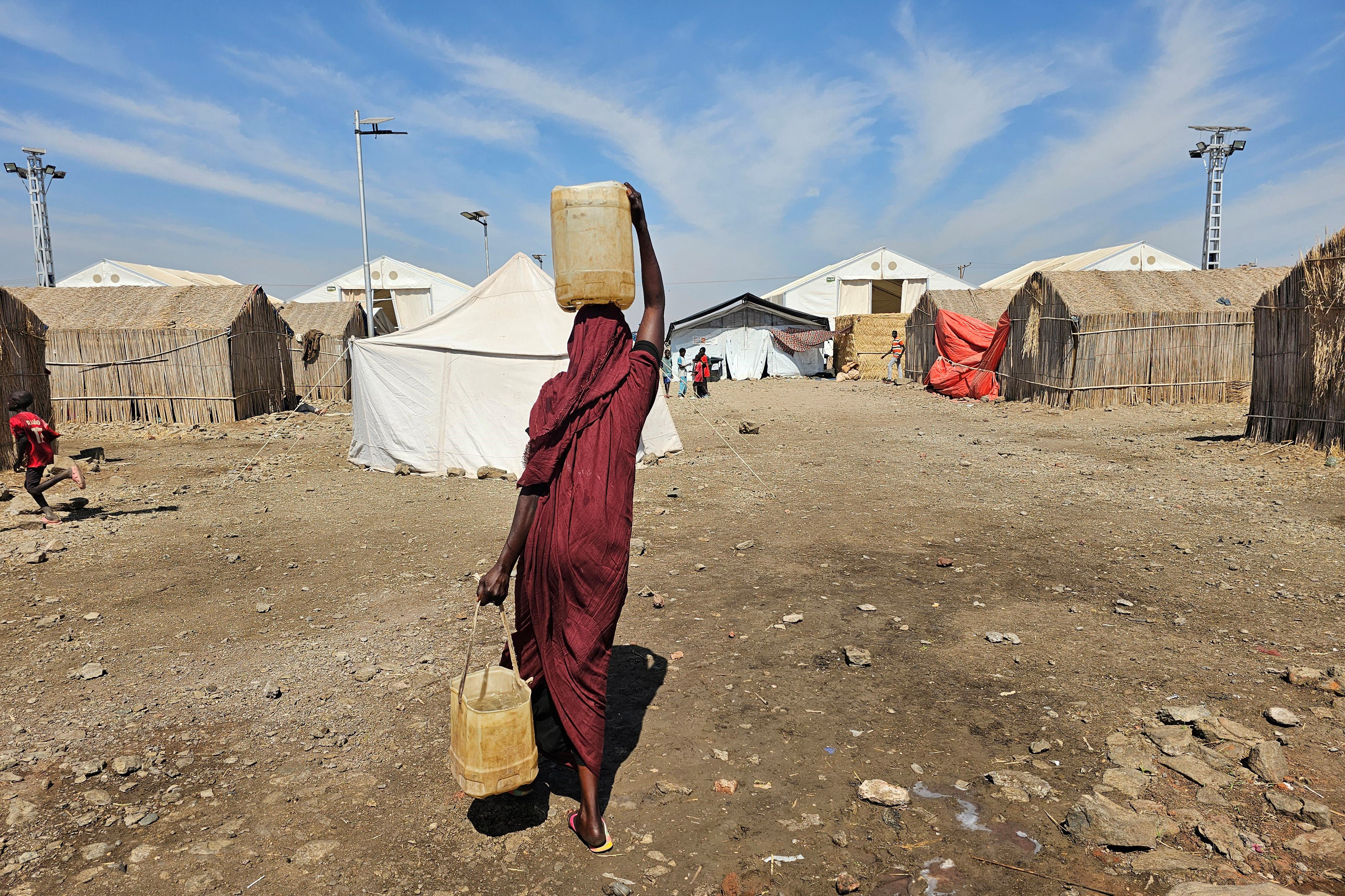 TOPSHOT - A displaced Sudanese woman carries plastic water containers at the Abu al-Naga displacement camp in the in Gedaref State, some 420km east of the capital Khartoum on February 6, 2026.