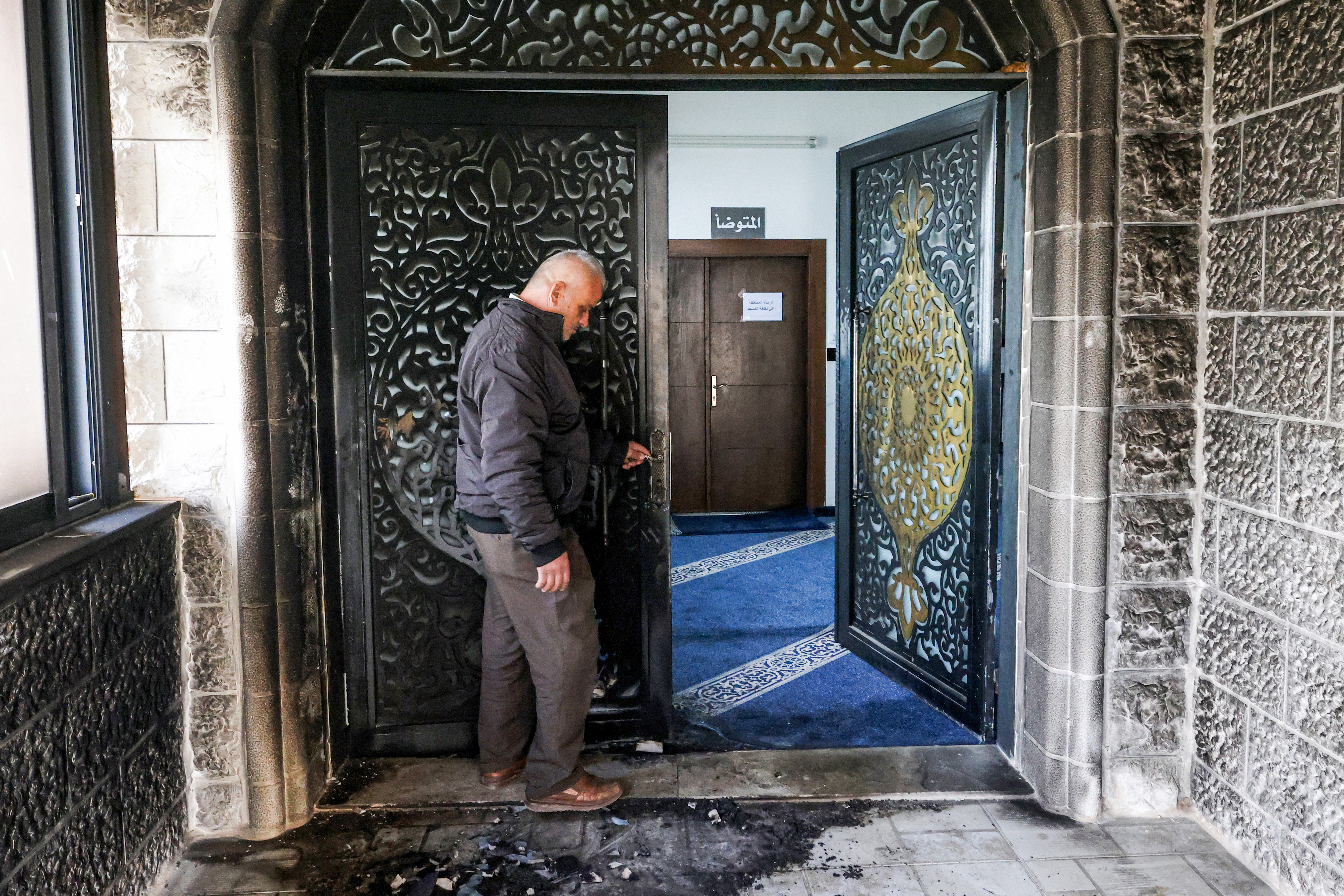 A man inspects the burnt entrance to the Abu Bakr al-Siddiq Mosque in the village of Tell, west of Nablus in the occupied West Bank, on February 23, 2026 following a reported attack by Israeli settlers.