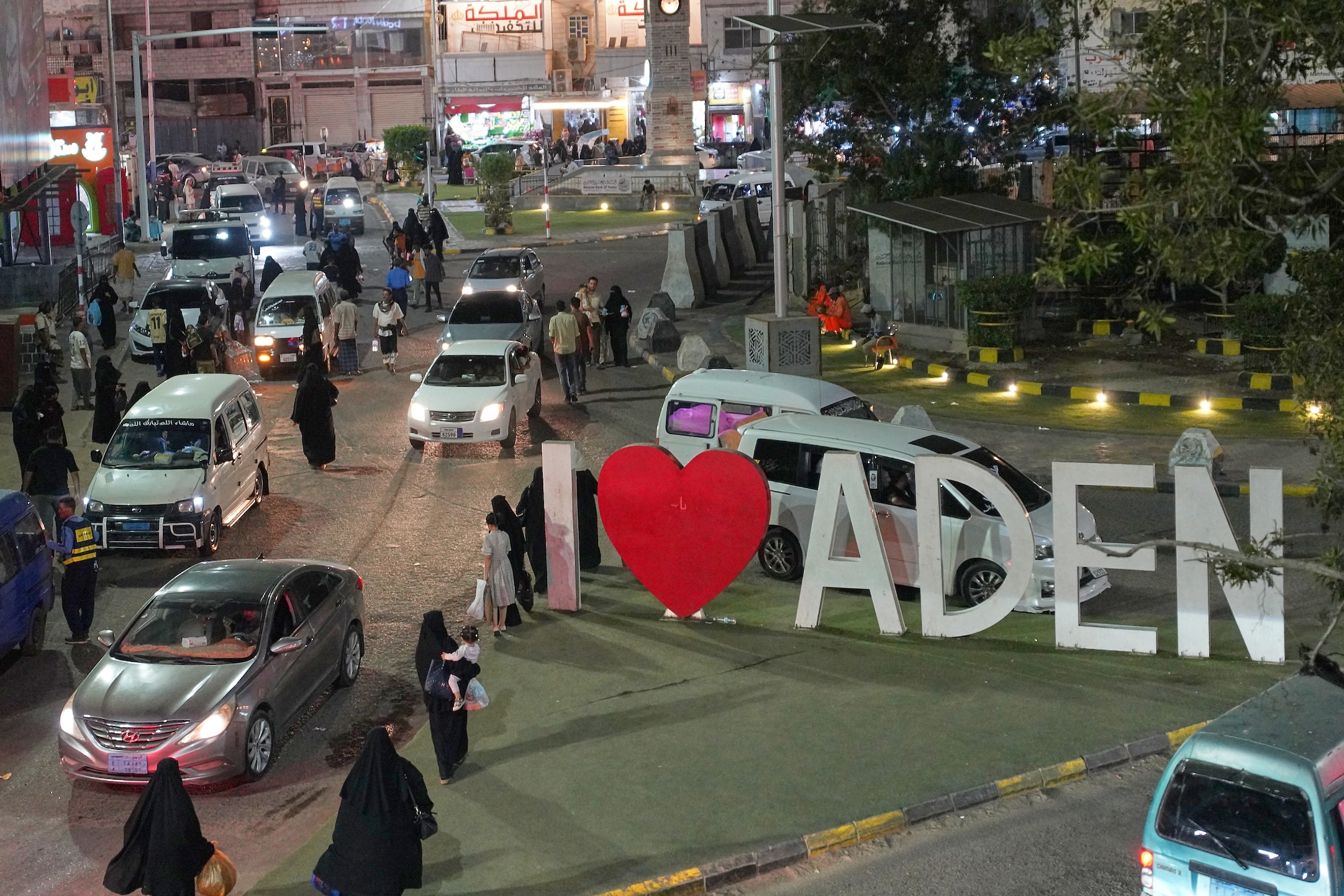 People shop in a busy street near a 'I love Aden' sign.