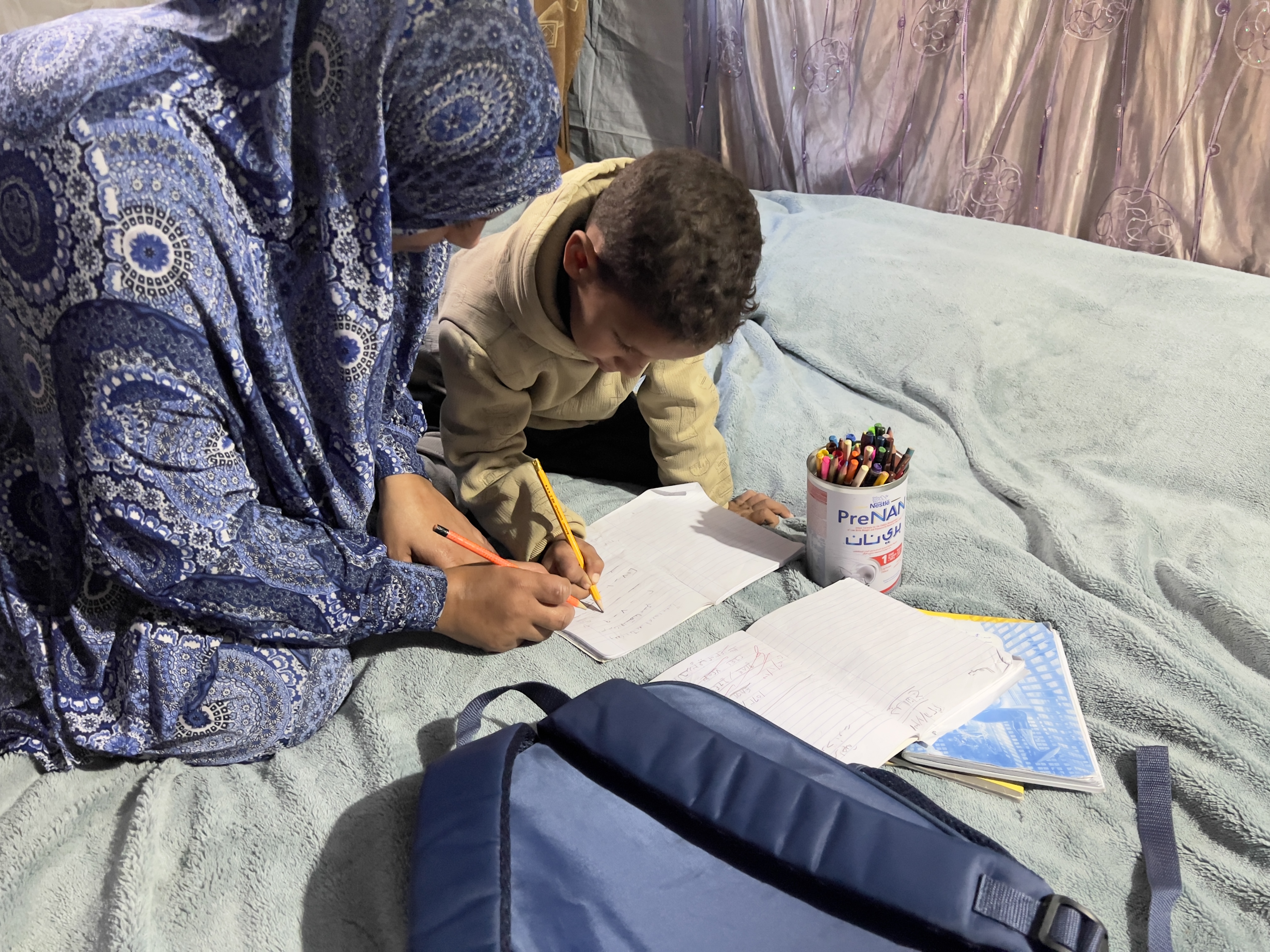 Nibal Abu Armana teaching her son Muhammed in their displacement tent in Nusairat Camp [Ola Al-Asi/ Al Jazeera]