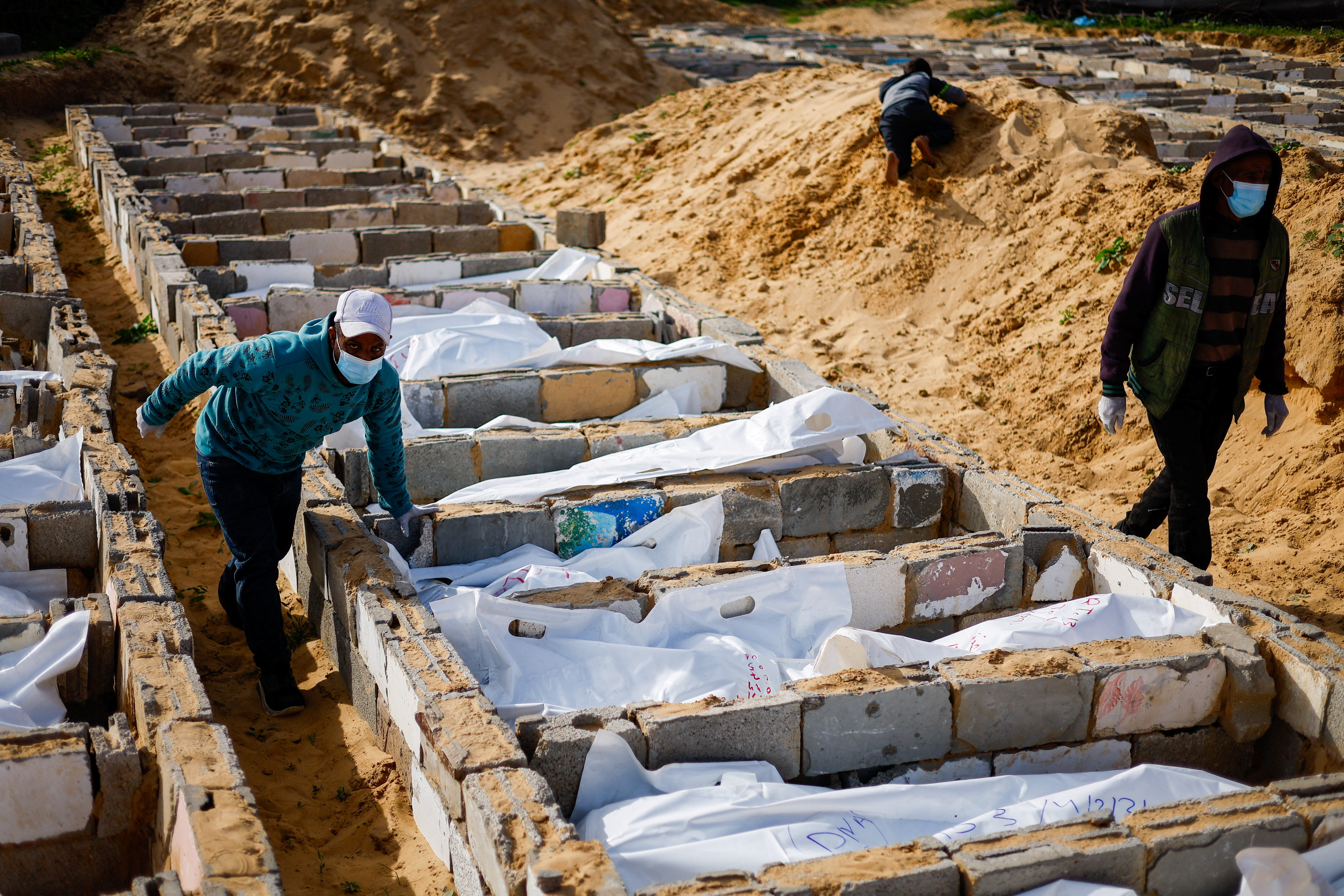 People walk next to bodies during a mass burial of unidentified Palestinians, whose bodies were released after being held in Israel during the war, in Deir Al-Balah, in the central Gaza Strip, February 13, 2026. REUTERS/Mahmoud Issa