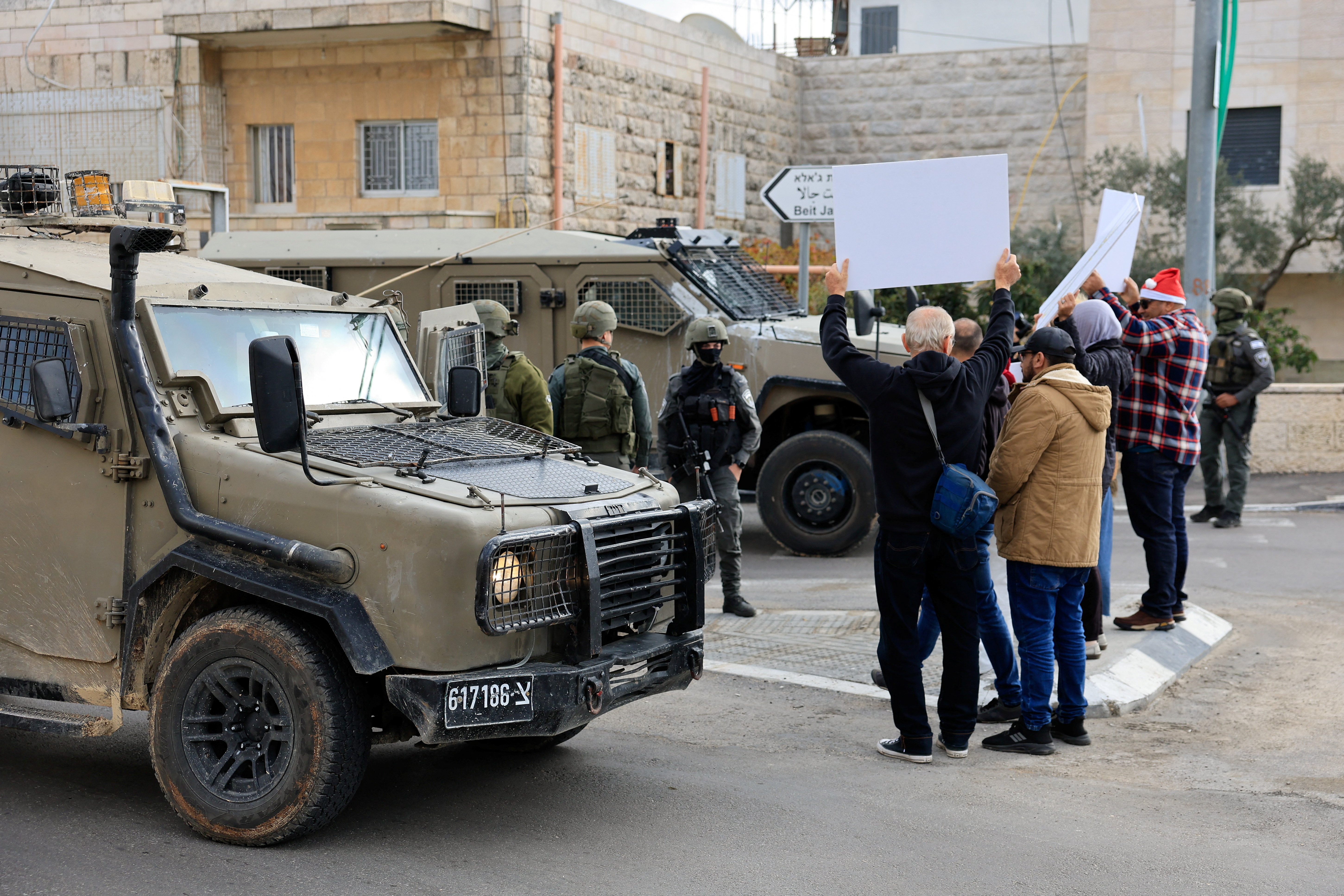 Palestinian and Israeli activists hold signs next to Israeli forces and military vehicles, during a protest against an Israeli draft law that would mandate the death penalty for Palestinian militants convicted of killing Israeli citizens