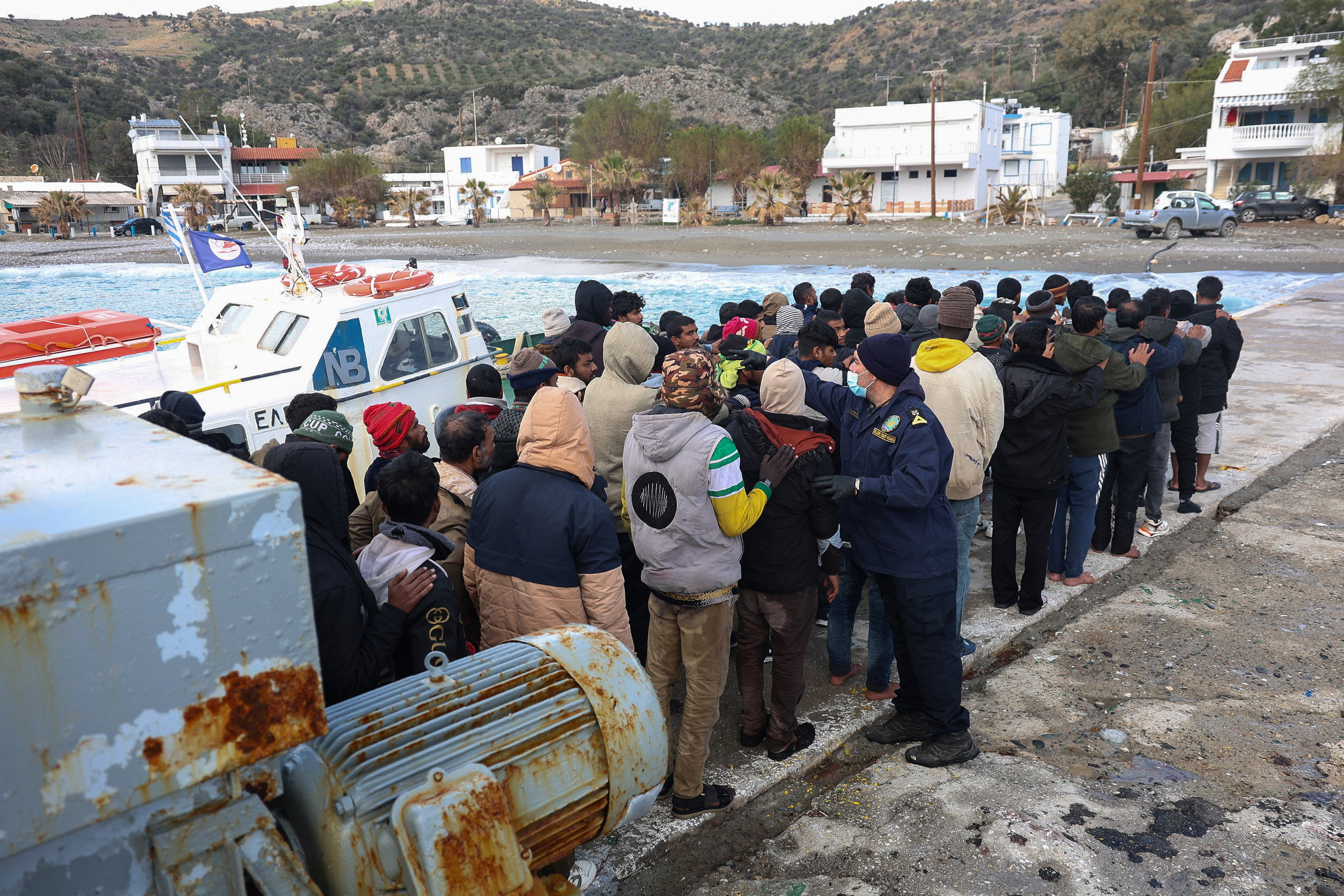 Migrants stand in line as a Greek coastguard officer counts them.