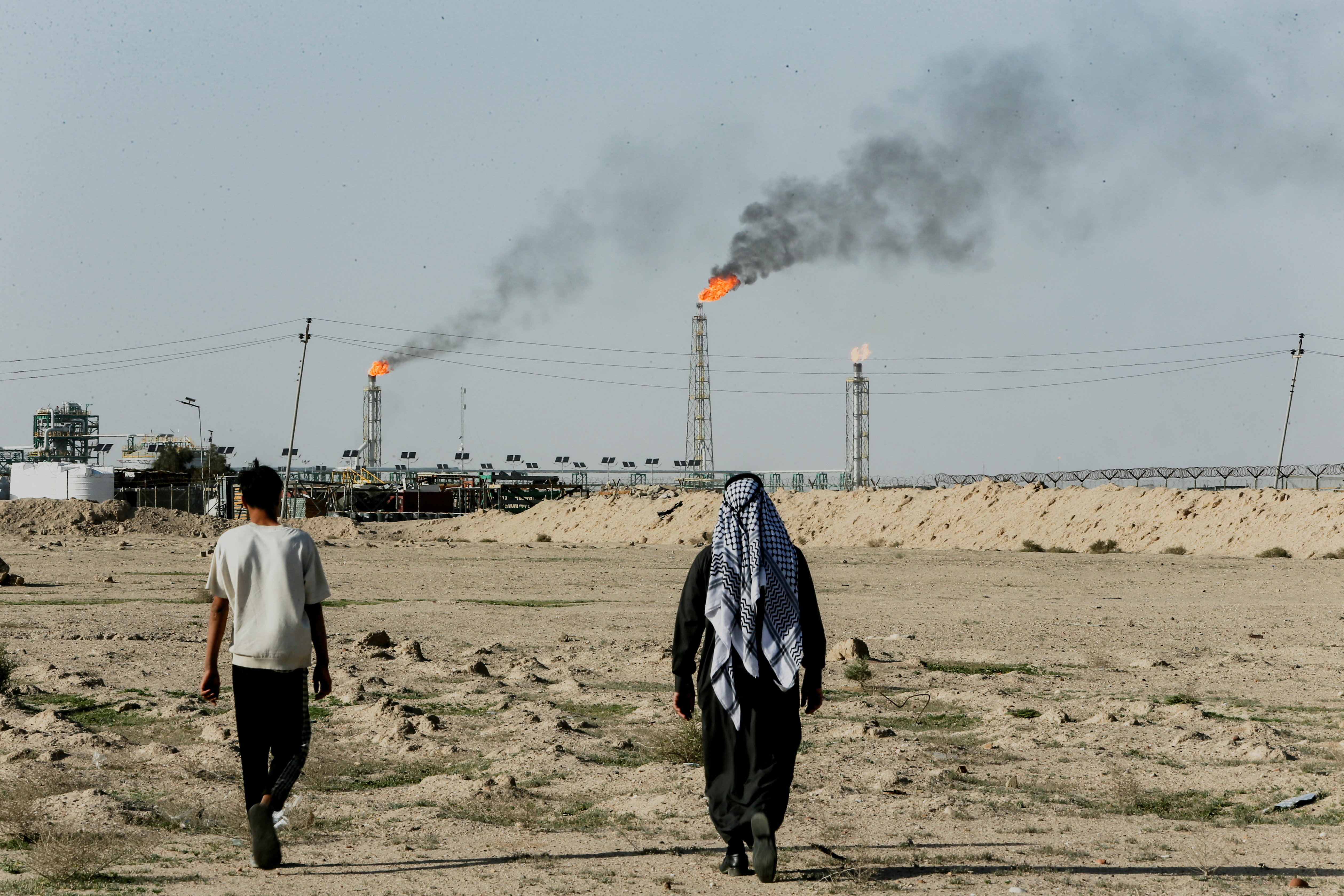 People walk near farmland by the Zubair oil field as gas flares rise in the distance, in Zubair Mishrif, Basra, Iraq, amid regional tensions following the recent disruption to shipping in the Strait of Hormuz and the U.S.-Israeli conflict with Iran, March 9, 2026. [Essam al-Sudani/Reuters]