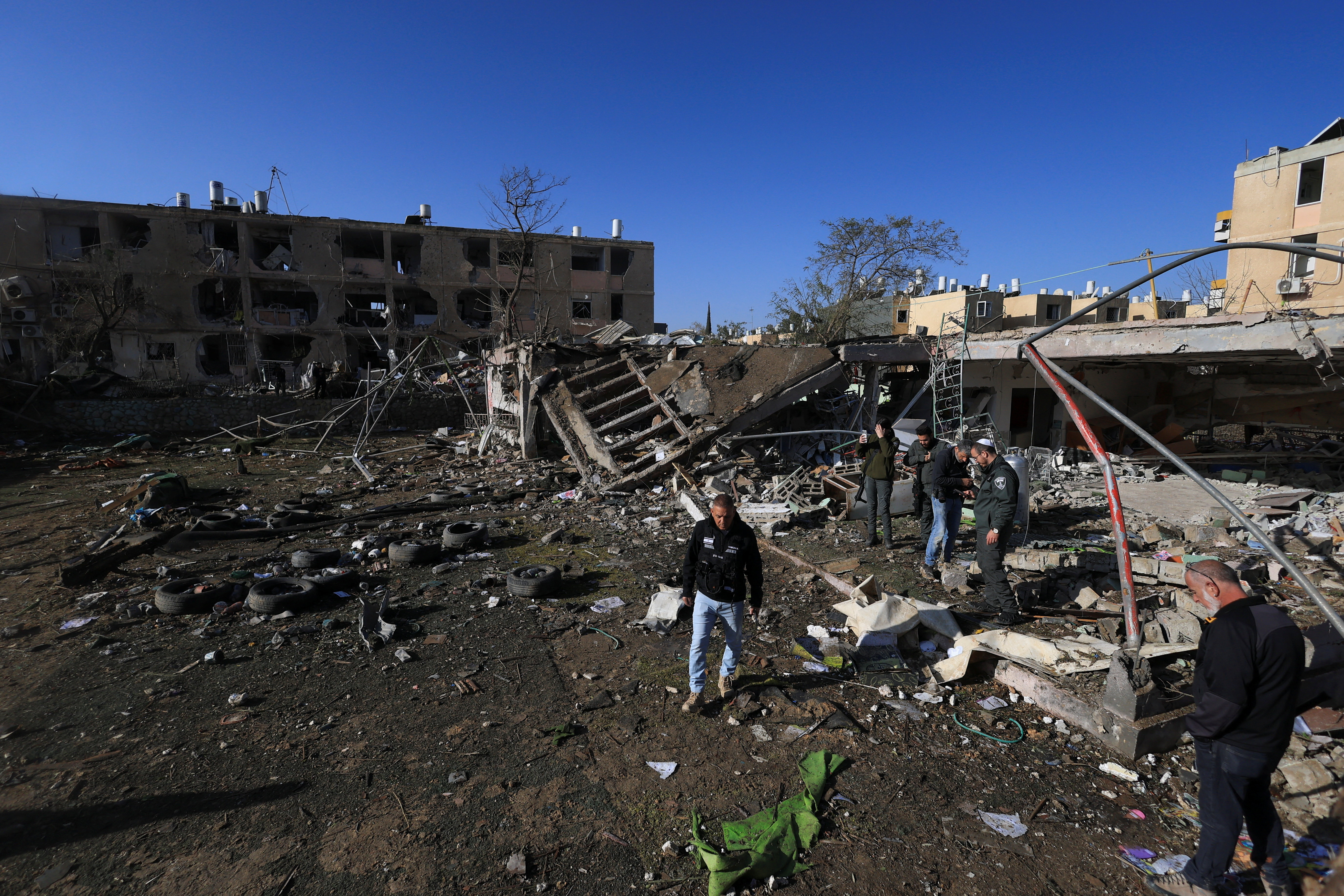 People, including Israeli security personnel, stand at a damaged area following a night of Iranian missile strikes which injured