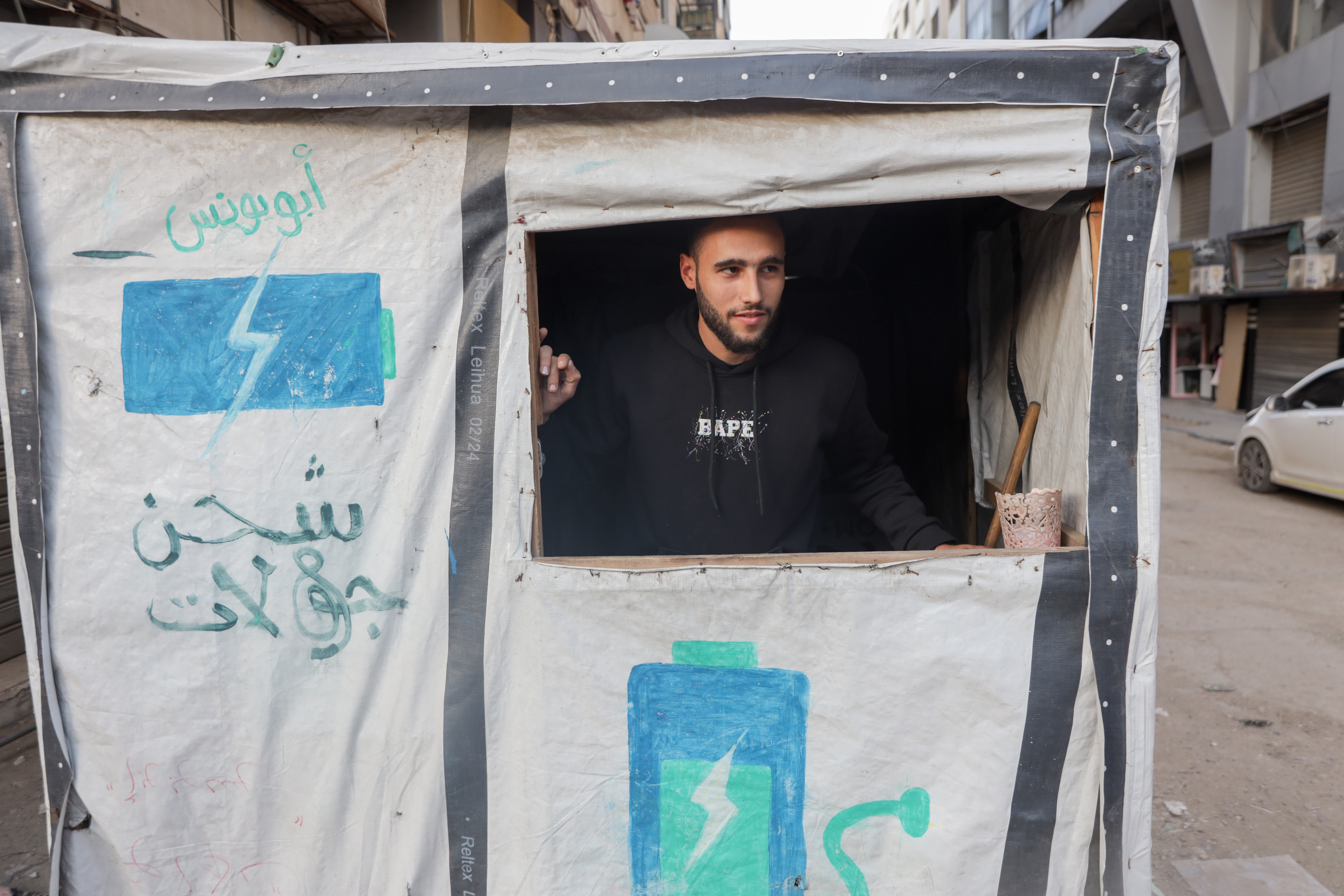 Abdulrahman Al-Awadi, a fine arts graduate, sits in a tent he set up as a mobile phone charging point for a small fee, amid the lack of opportunities in Gaza after the war [Abdelhakim Abu Riash/ Al Jazeera]