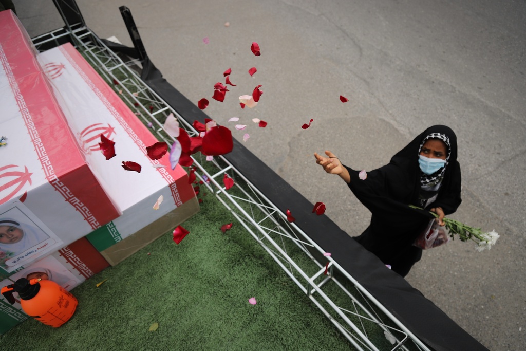 Woman throws rose petals at coffins