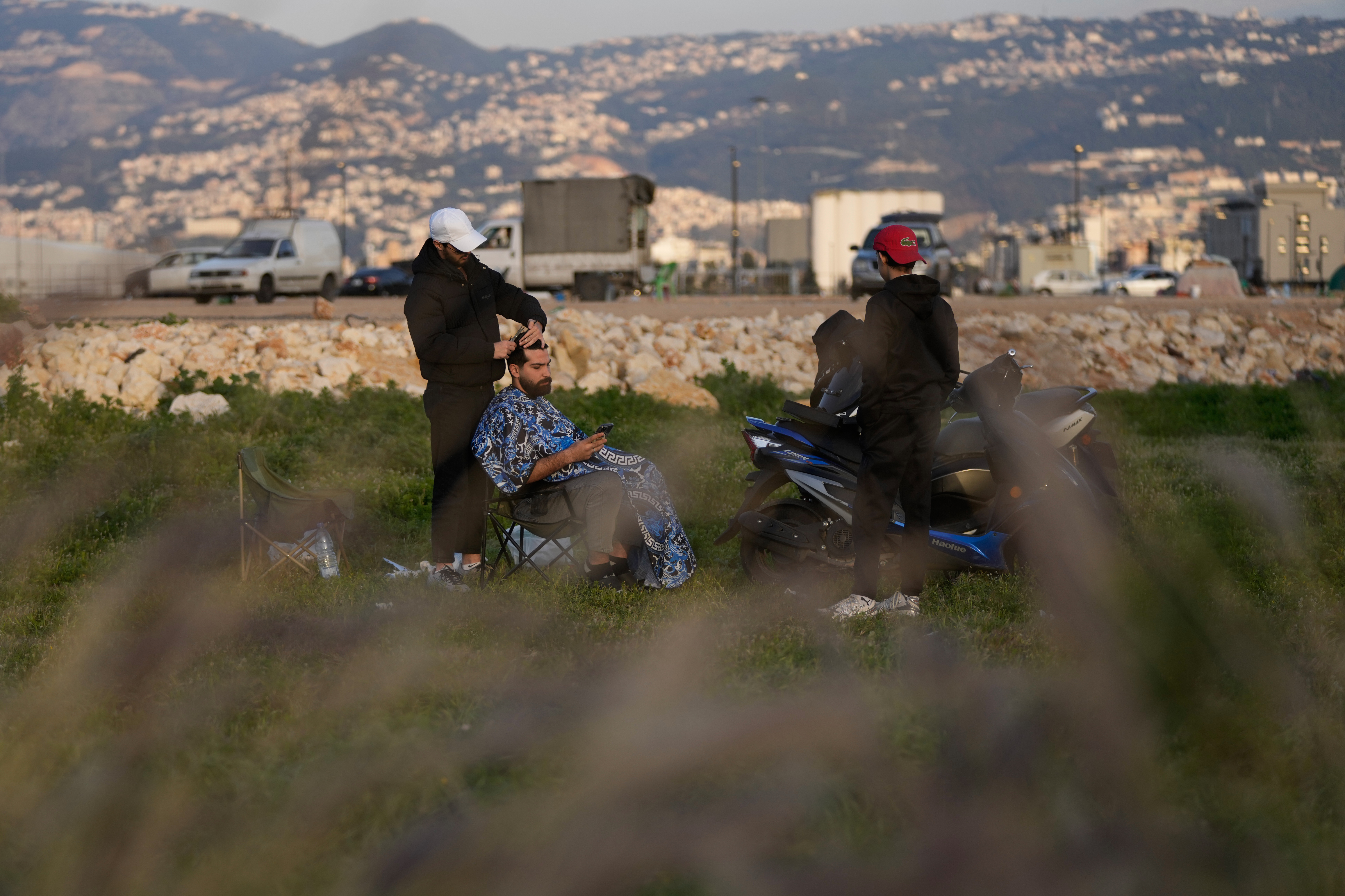 Amir Hajj, left, a barber displaced by Israeli airstrikes in Dahiyeh, Beirut's southern suburbs, cuts a customer's hair at Beirut's seaside promenade along the Mediterranean Sea in Beirut,