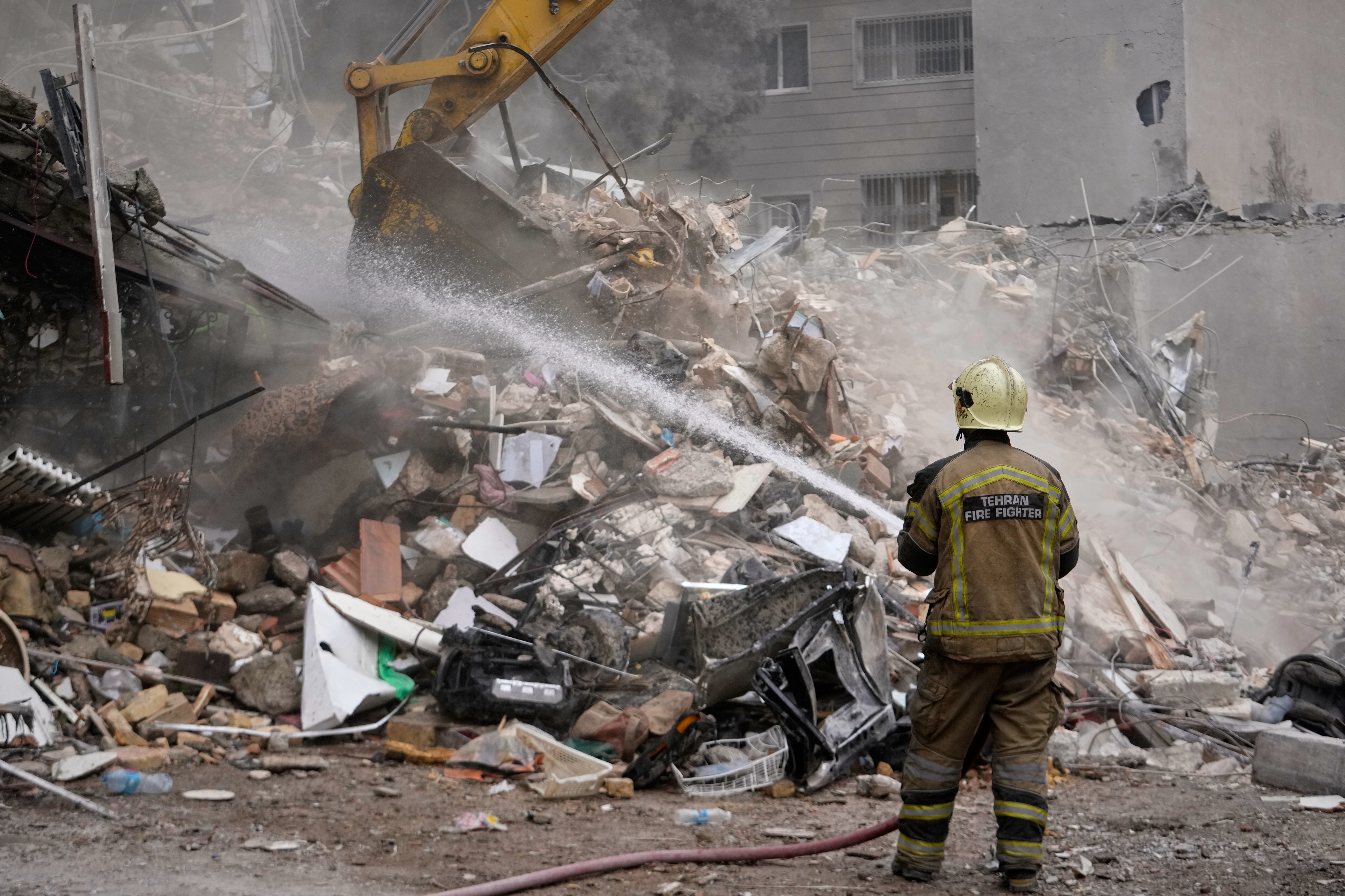 A firefighter hoses down smoldering rubble as a bulldozer clears debris at a residential building hit in an earlier U.S.-Israeli strike in Tehran, Iran, Monday, March 23, 2026. (AP Photo/Vahid Salemi)