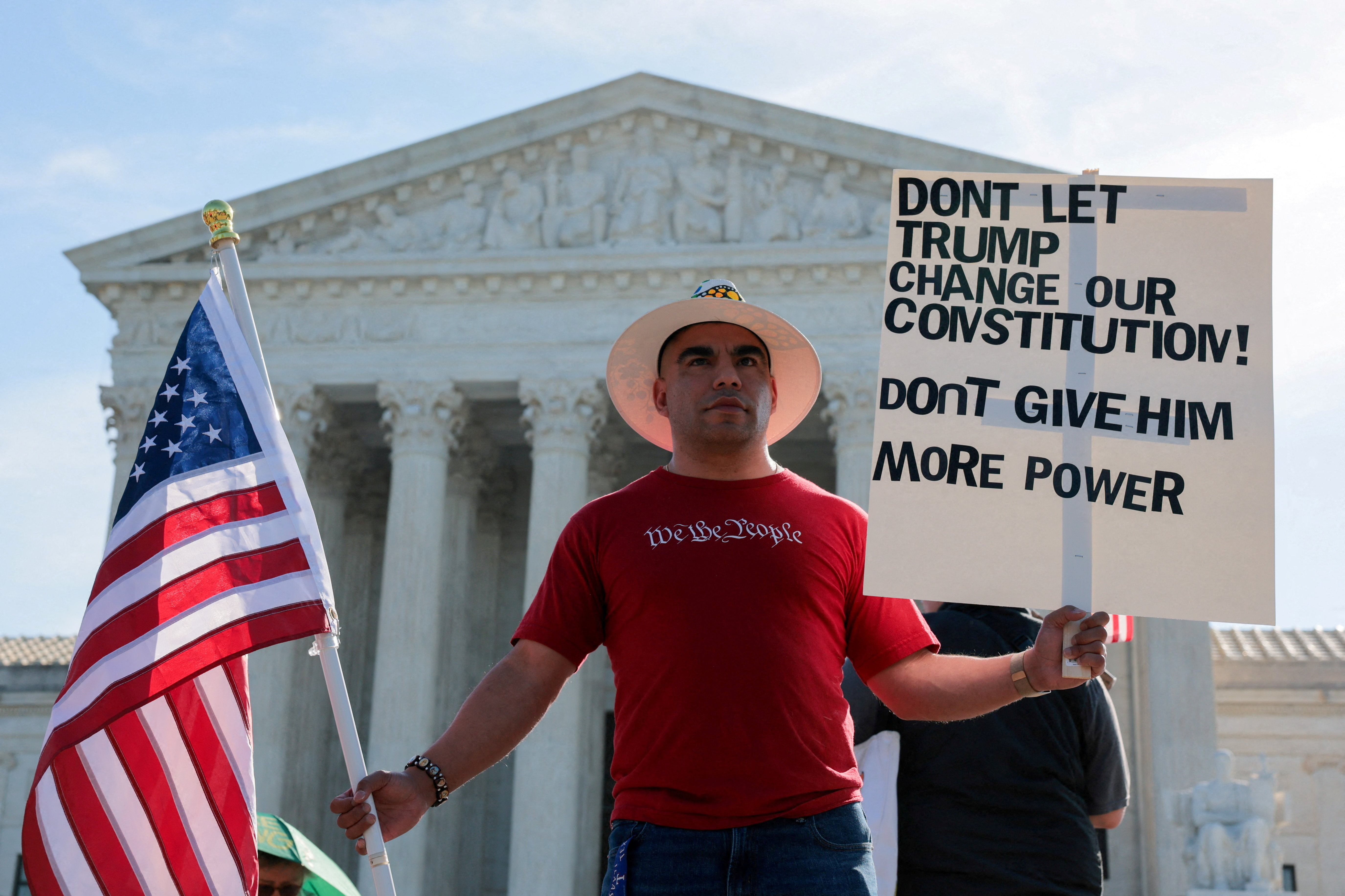 A demonstrator wearing a T-shirt with the phrase "We the people" holds a sign and a U.S. flag outside the U.S. Supreme Court building on the day the court is expected to hear oral arguments on the legality of the Trump administration's effort to limit birthright citizenship for the children of immigrants, in Washington, D.C., U.S., April 1, 2026. REUTERS/Kylie Cooper TPX IMAGES OF THE DAY