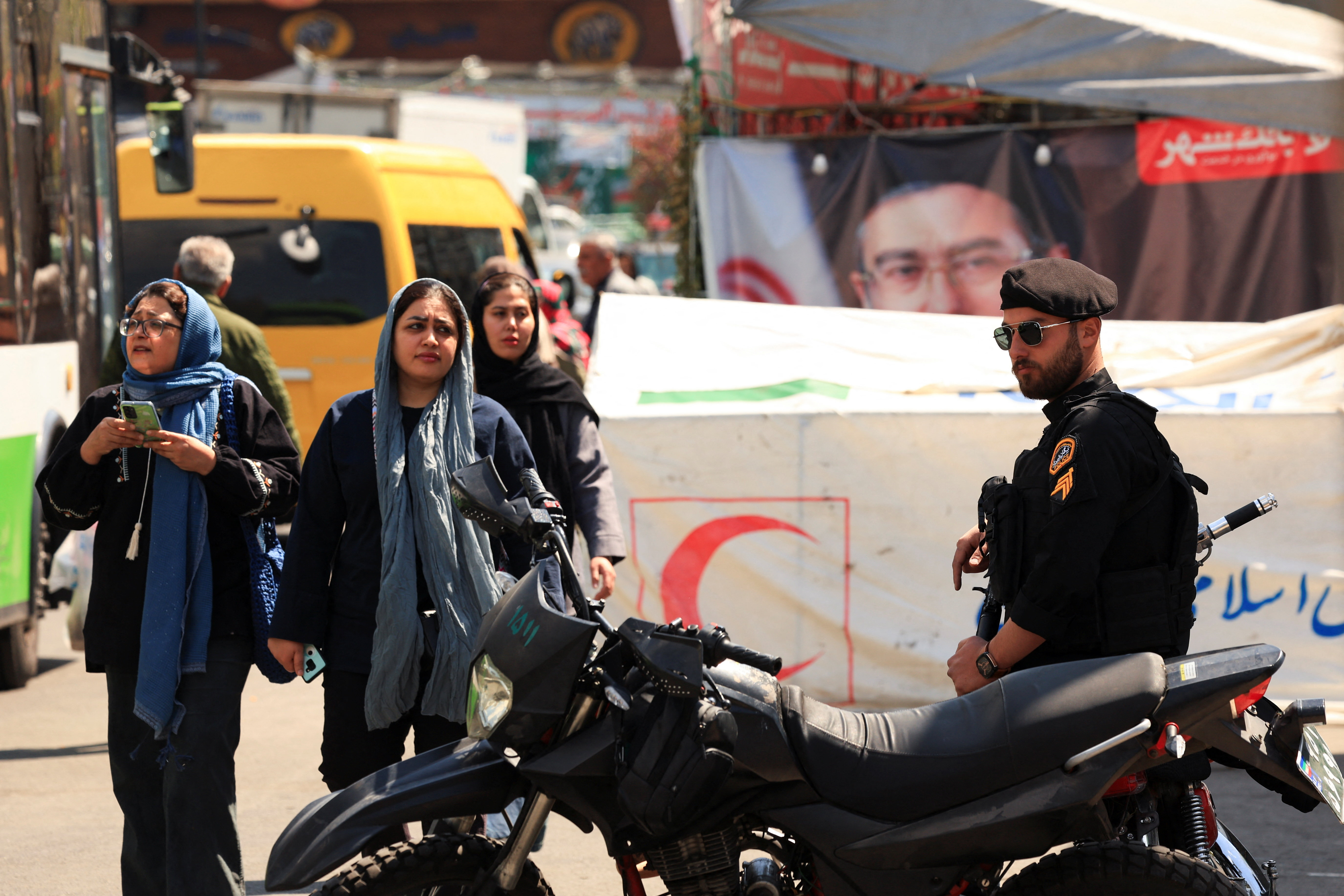 Iranian women walk past a police officer in a busy street