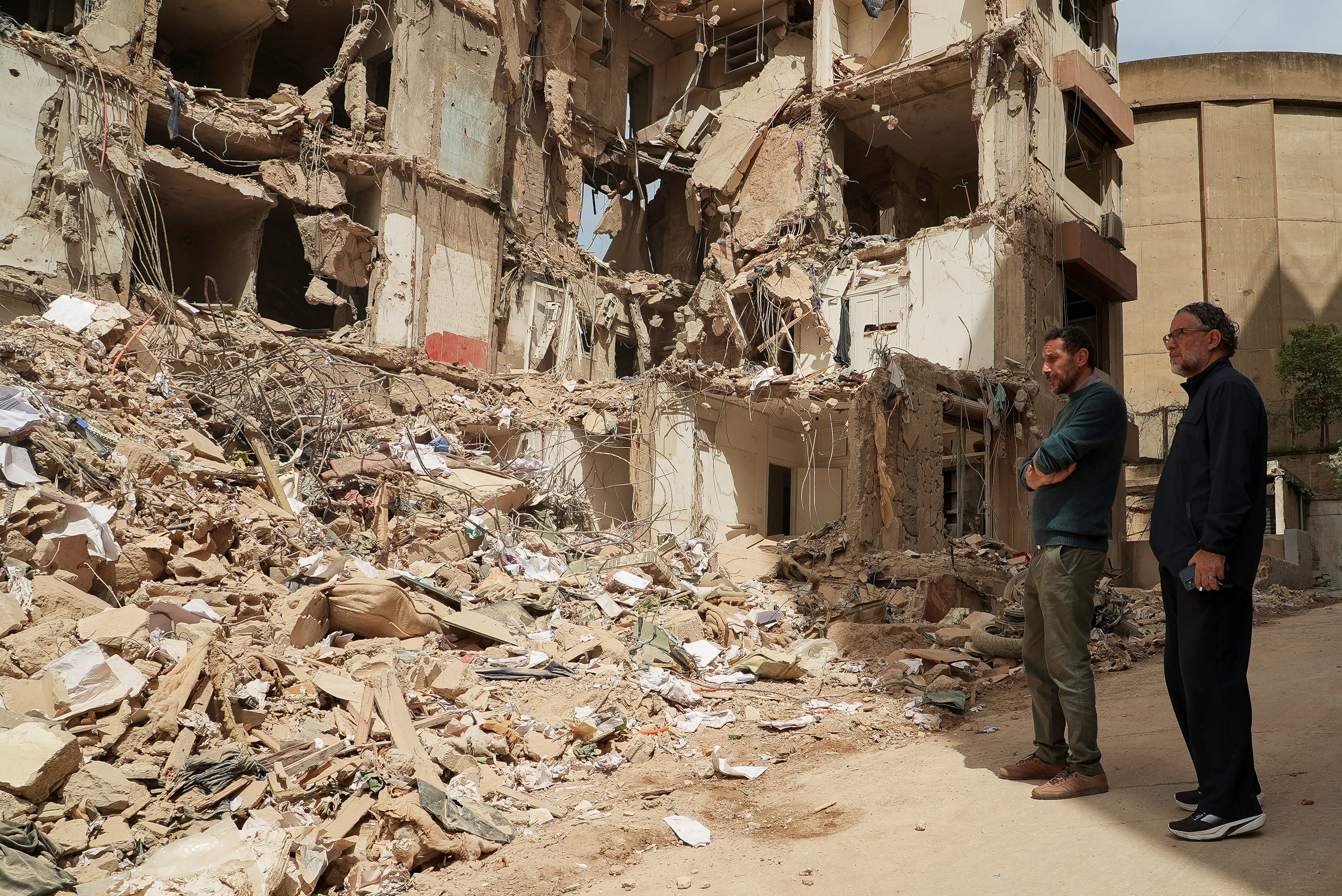 Two men stand at the site of a destroyed apartment building.