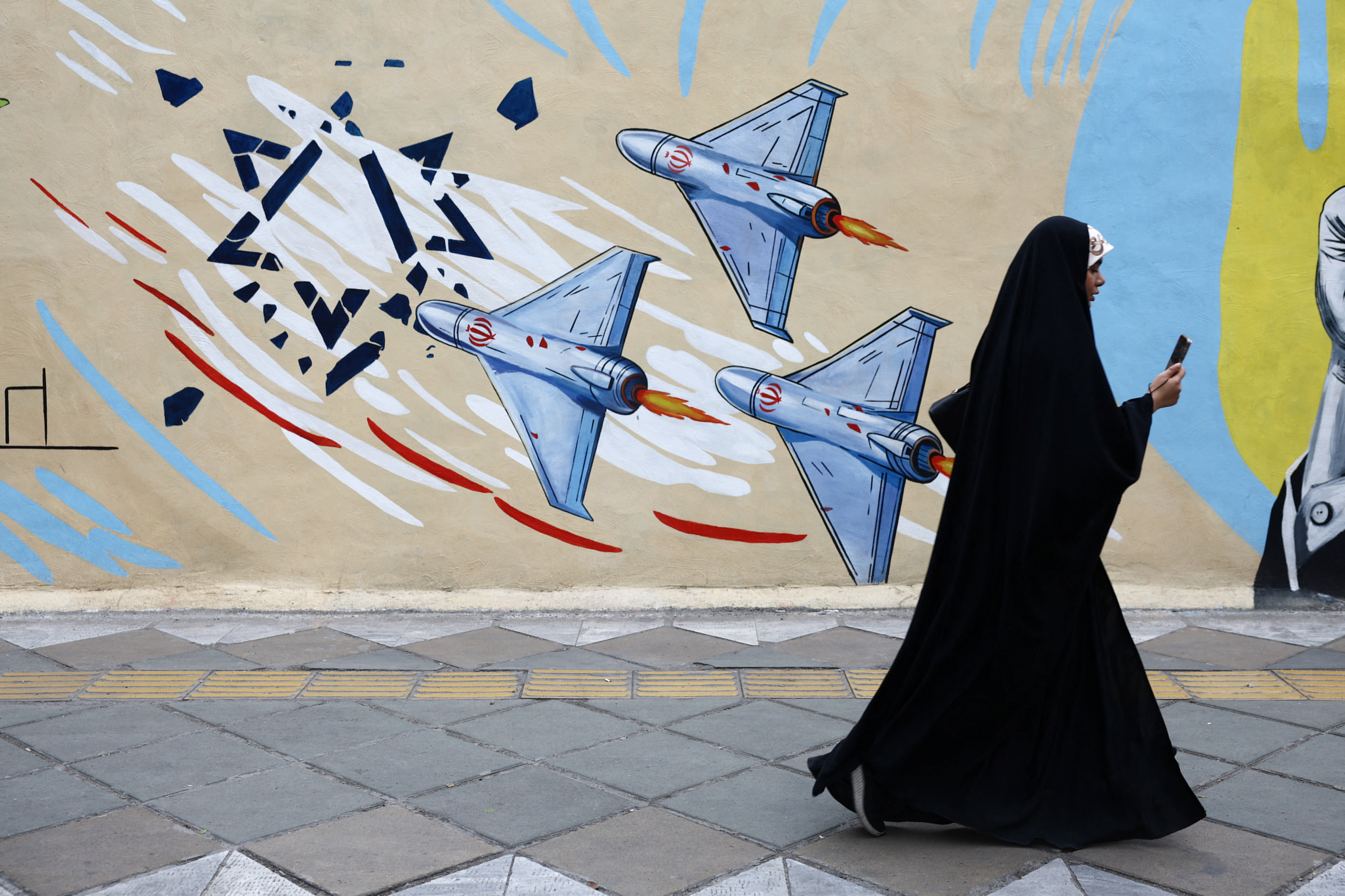 A woman walks next to an anti-Israeli mural on a street, amid a ceasefire between U.S. and Iran,