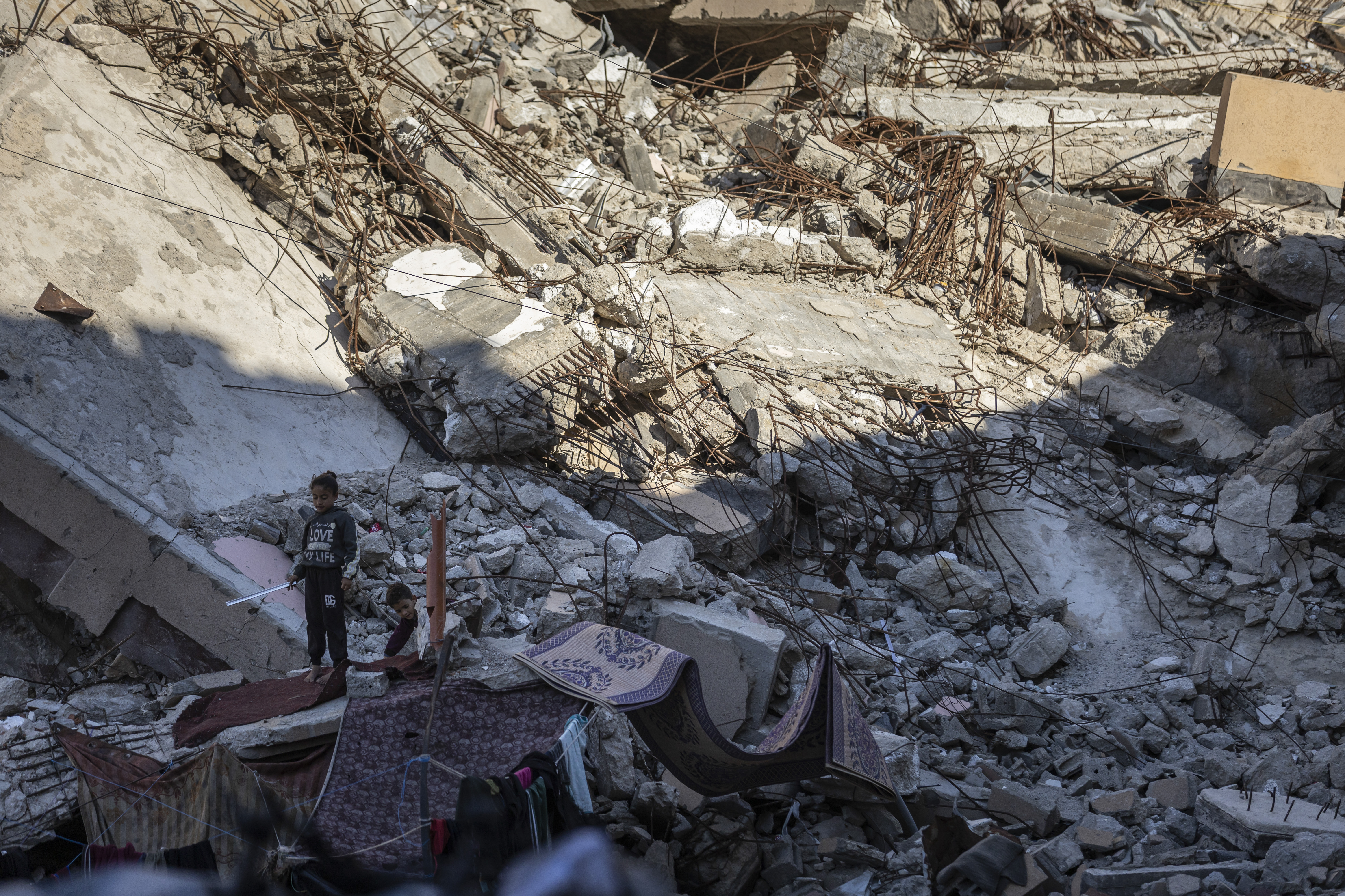 Two Palestinian children stand on the rubble of a destroyed building in Gaza, where they have set up a temporary shelter after being forcibly displaced.