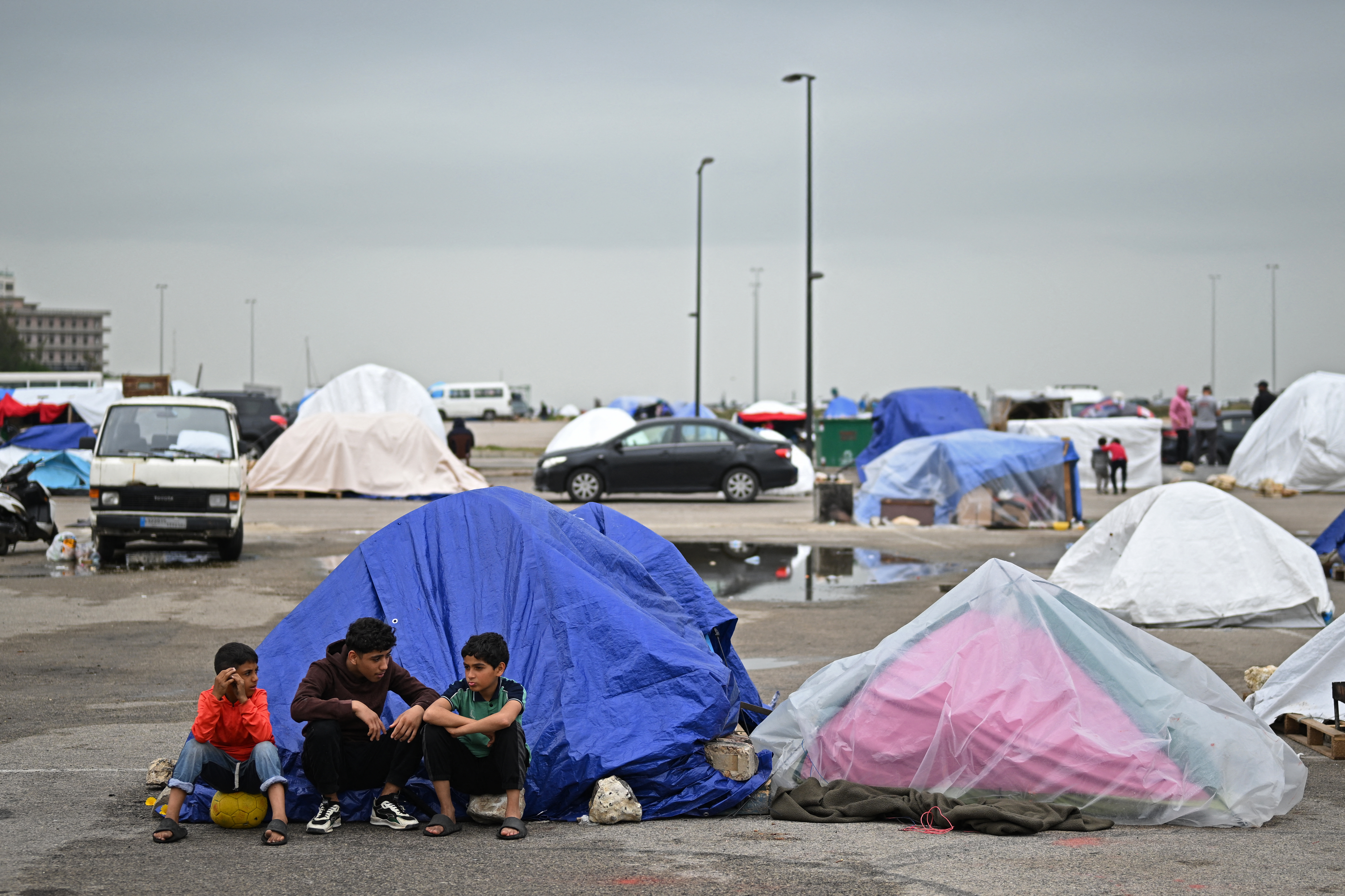 Displaced young boys sit at the entrance of a tent.
