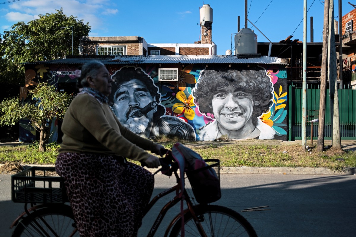 A woman rides a bicycle past murals depicting the late football star Diego Maradona.