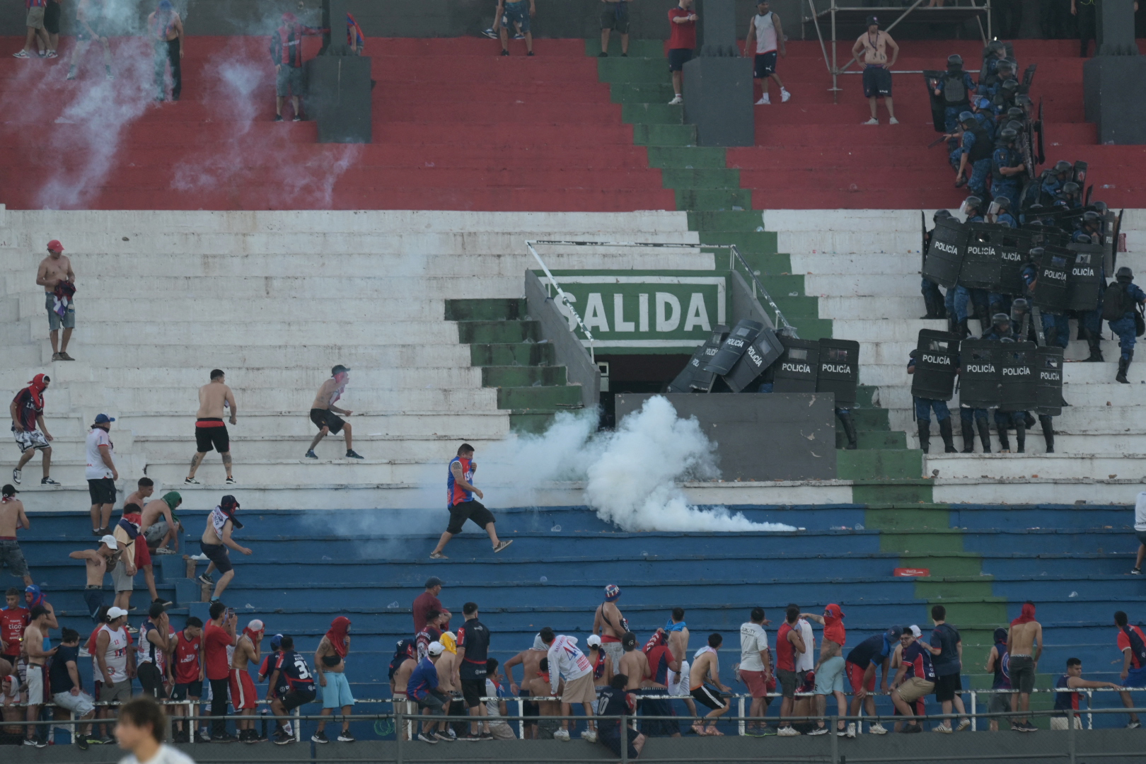 Fans of Cerro Porteno clash with police officers during the Paraguayan tournament football match between Olimpia and Cerro Porteno at the Defensores del Chaco stadium in Asuncion on April 19, 2026. Several people were injured and at least a hundred were arrested following incidents that occurred during the Paraguayan football derby between Olimpia and Cerro Porteno, which was suspended in the first half in Asuncion on April 19, 2026. (Photo by Daniel DUARTE / AFP)