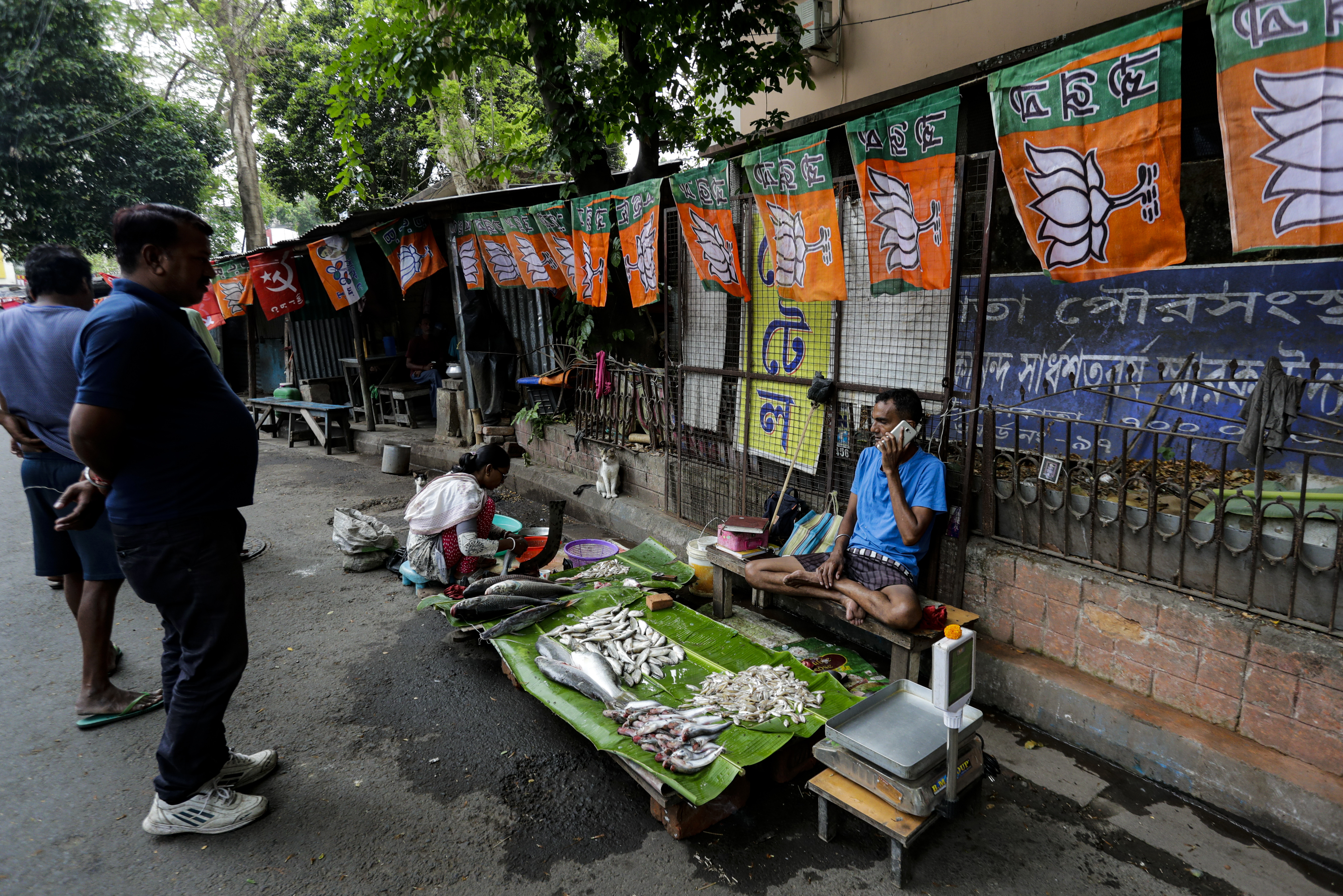 A fish vendor talks on his mobile phone at his roadside stall decorated with political party flags ahead of the West Bengal state elections in Kolkata, India, on Friday, April 9, 2021