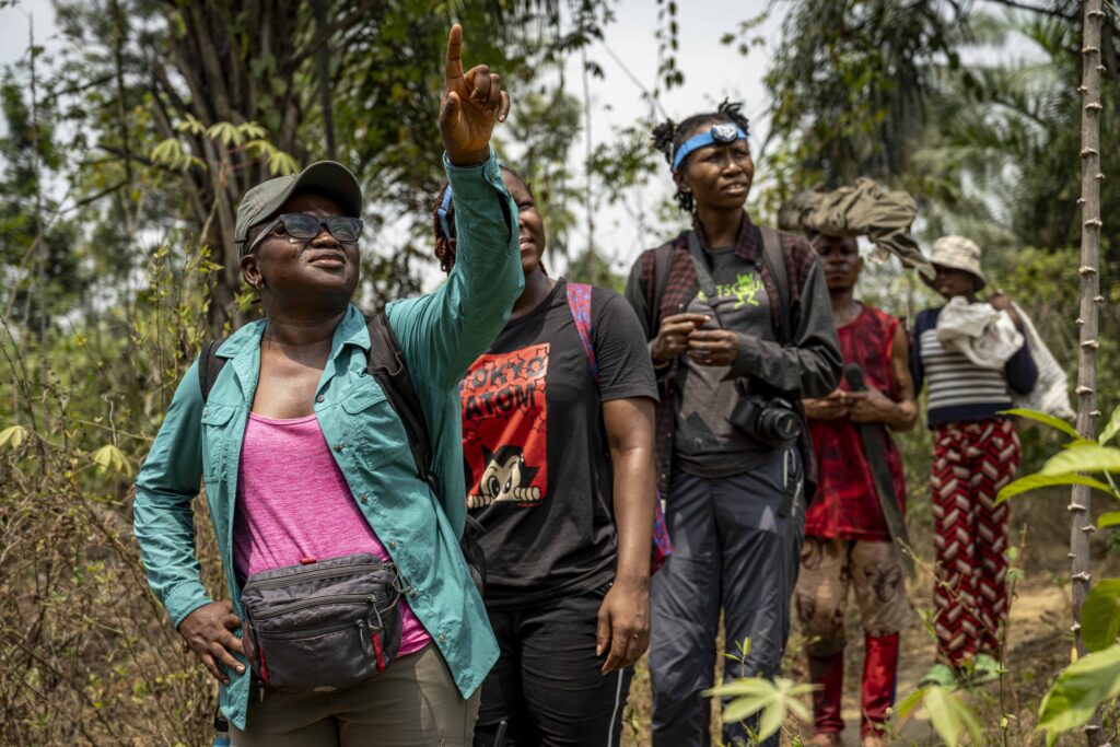 A woman wearing a teal jacket leads people through the forest
