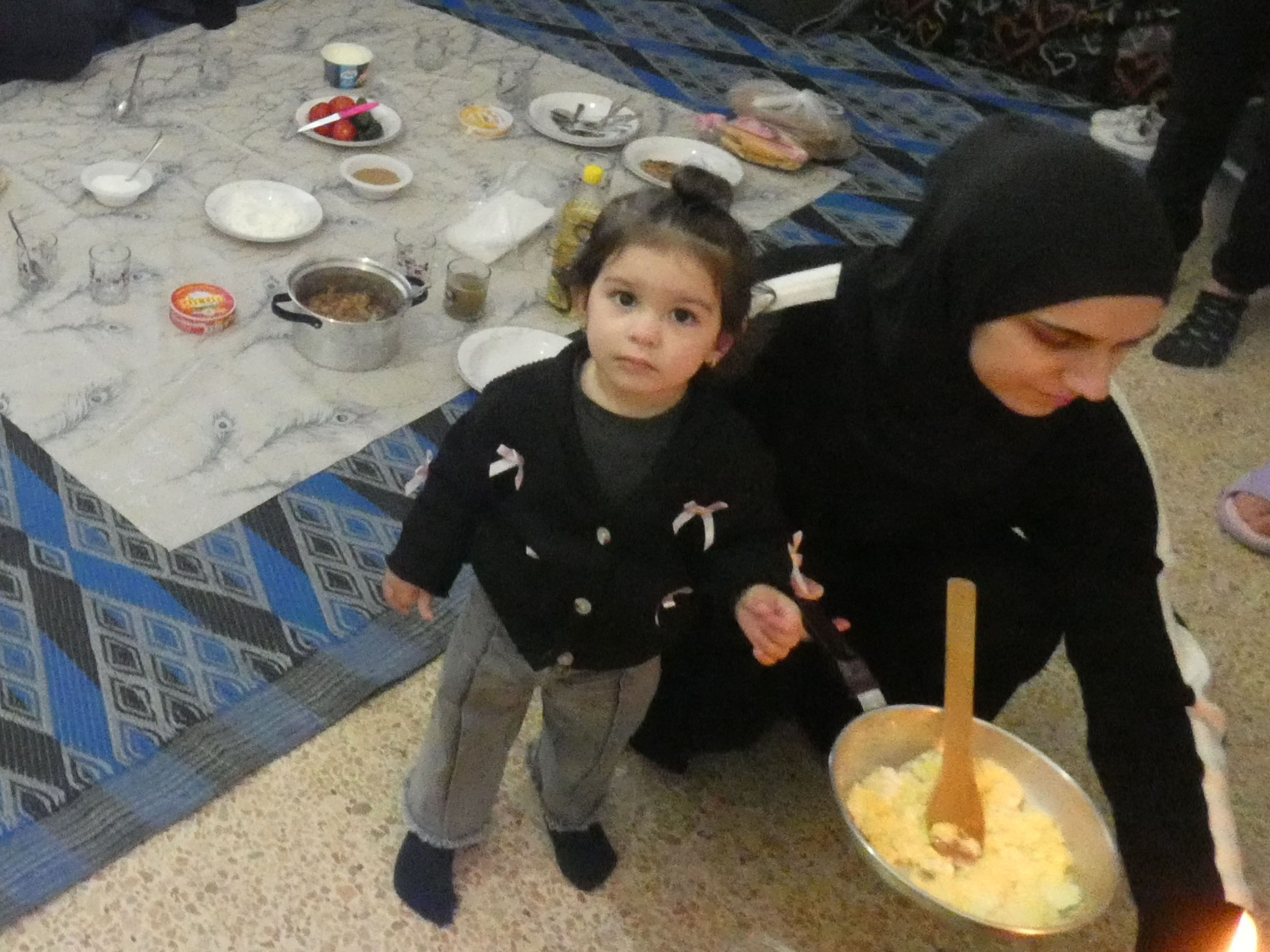 A mother and daughter share a meal on a classroom floor.