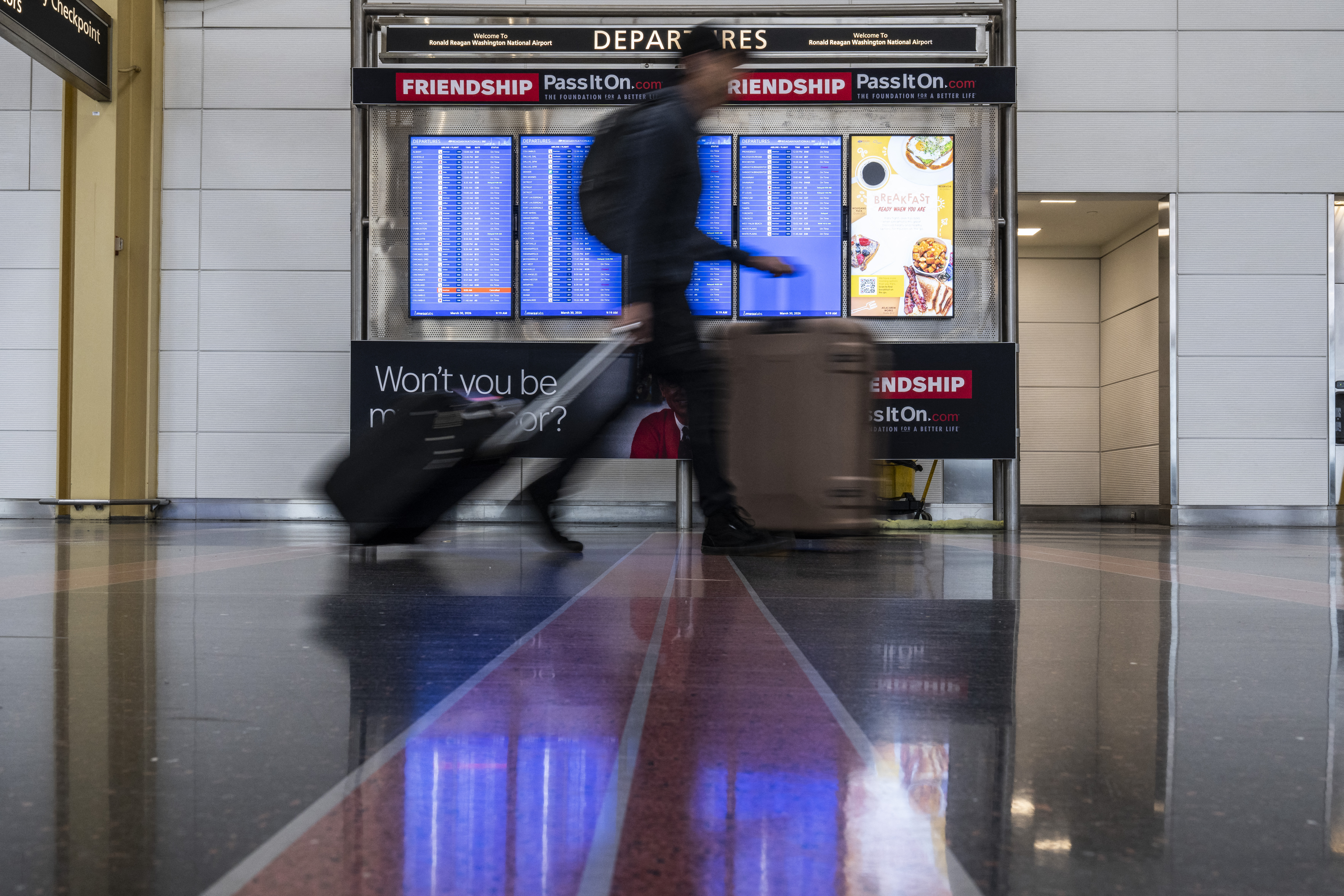 WASHINGTON, DC - MARCH 30: Travelers walk past screens giving updates on outbound flights at Ronald Reagan International Airport on March 30, 2026 in Washington, DC. Airports around the country started recovering from long lines as TSA Agents begin to receive their first paychecks after about 61,000 TSA employees had been working without pay since a partial government shutdown started February 14. Roberto Schmidt/Getty Images/AFP (Photo by ROBERTO SCHMIDT / GETTY IMAGES NORTH AMERICA / Getty Images via AFP)