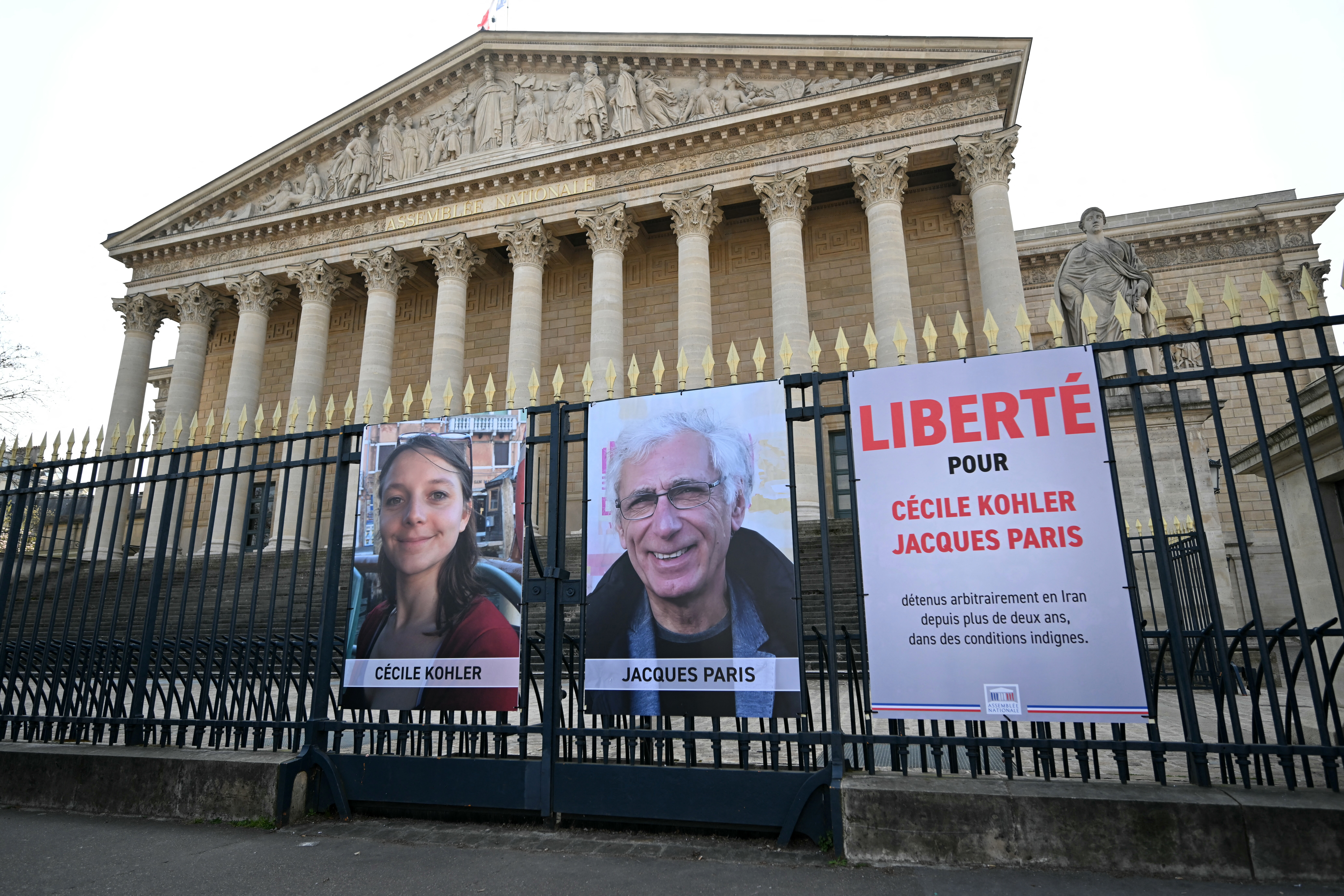 (FILES) This photograph shows the newly displayed portraits of French national Cecile Kohler (L) currently imprisoned in Iran with her partner French national Jacques Paris (C) along with a placard reading "Freedom for Cecile Kohler and Jacques Paris arbitrarily detained in Iran for over two years in appalling conditions" outside the Palais Bourbon, France's National Assembly, following their meeting with the President of France's National Assembly, in Paris, on March 25, 2025.