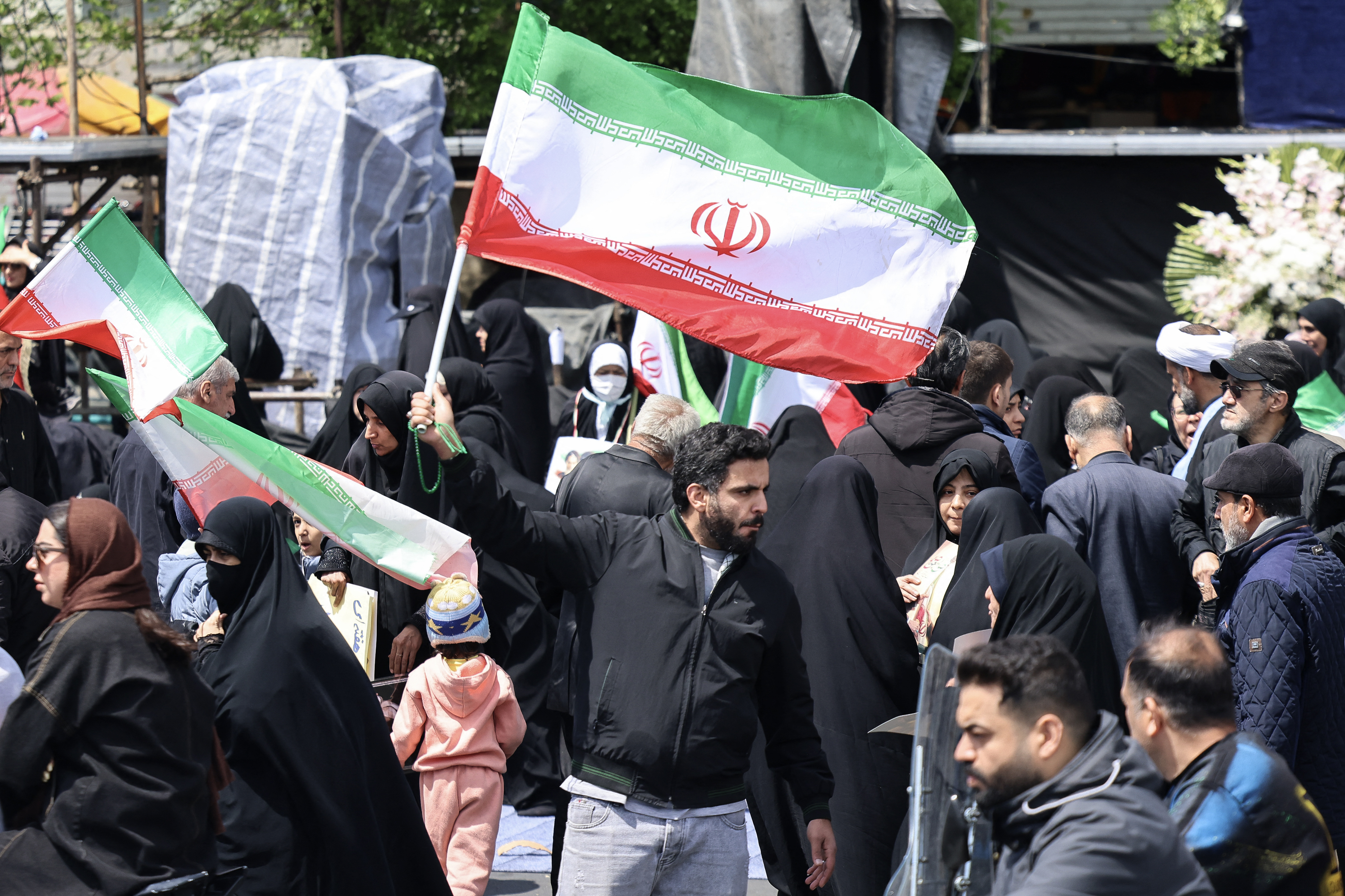 An Iranian man waves the national flag as people gather in Tehran's Revolution Square after the United States and Iran agreed to a two-week ceasefire, on April 8, 2026.
