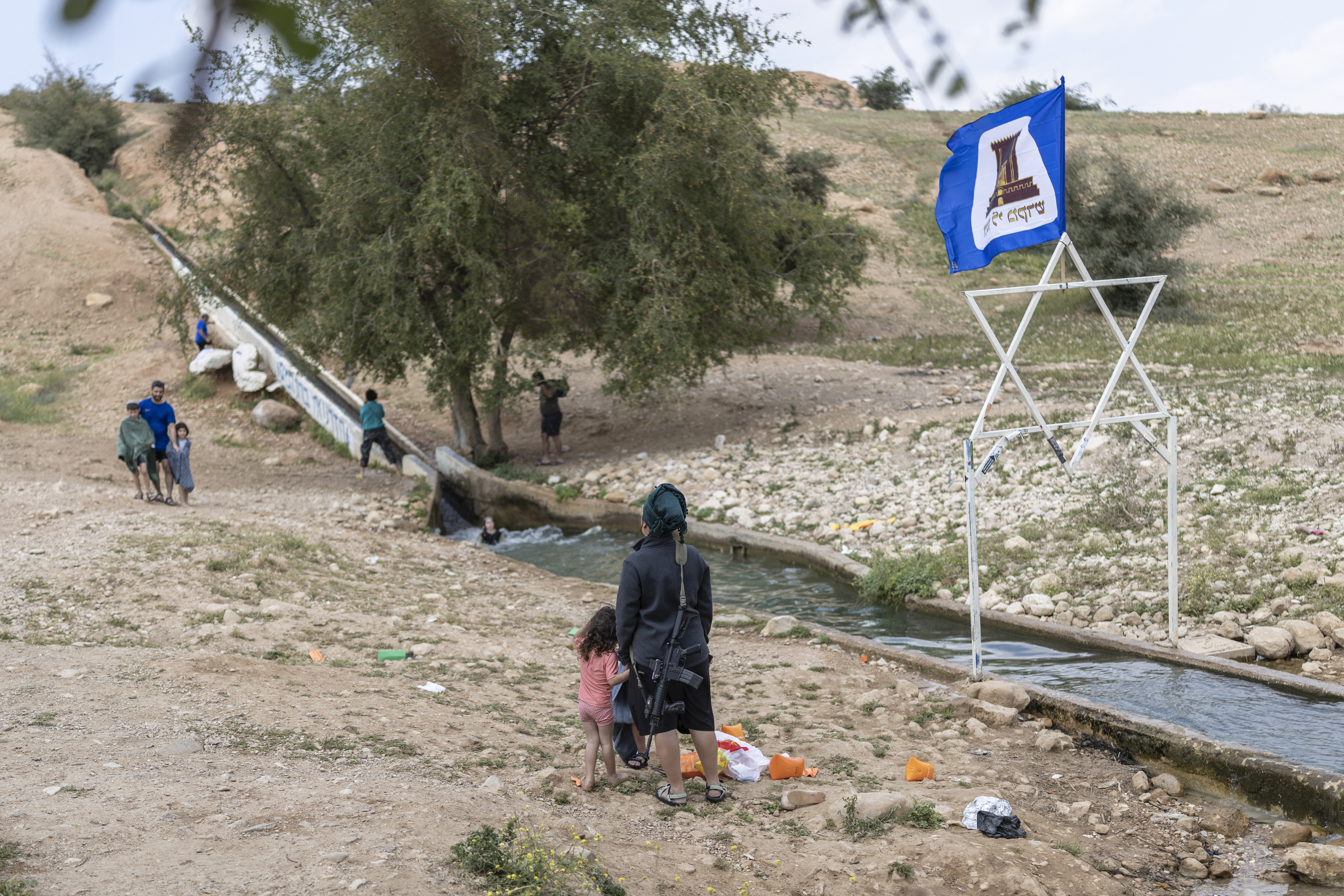An armed Israeli settler gathers with others at a water slide.