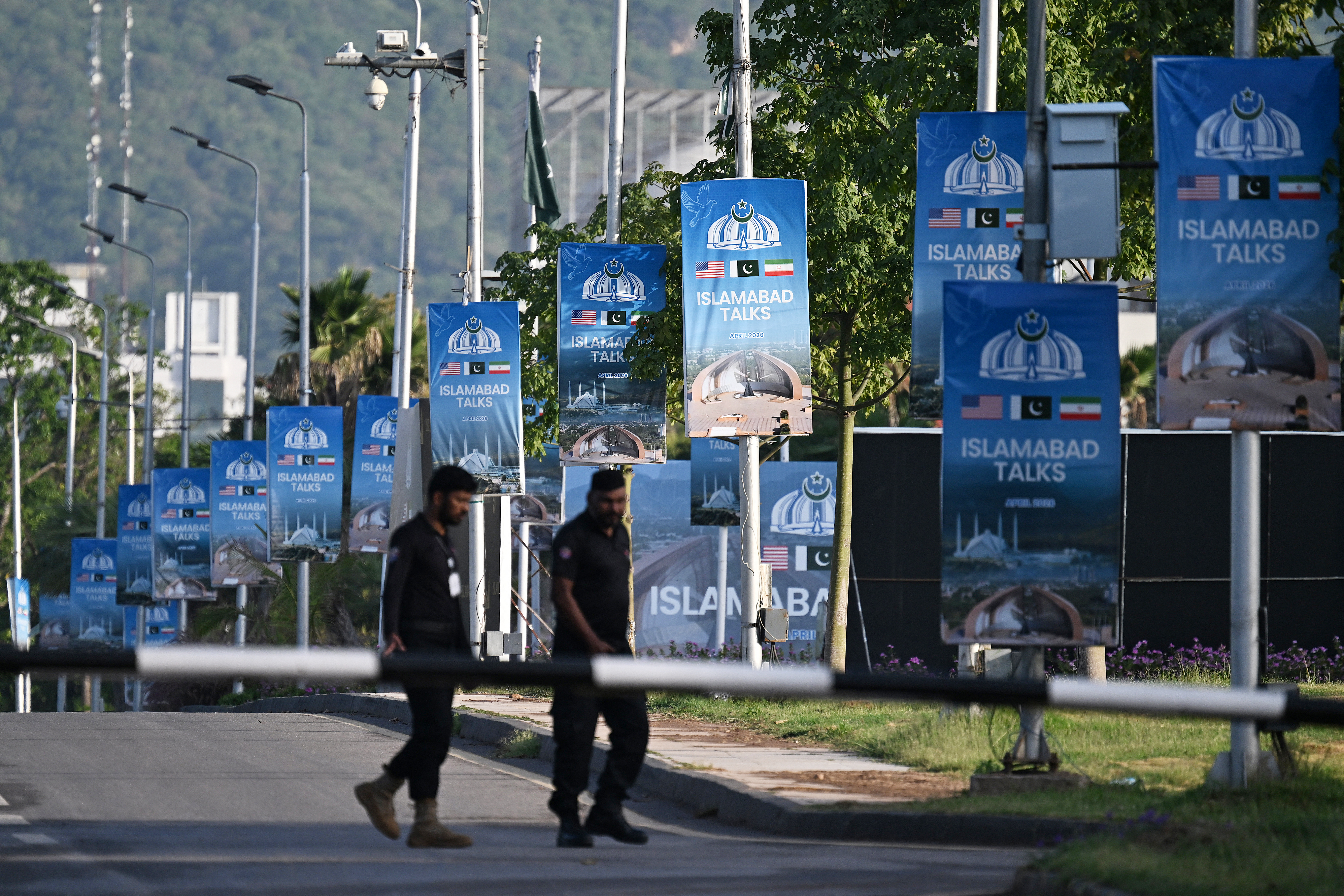 Police officers walk past posters highlighting Pakistan's mediation of Iran–US peace talks near the Serena Hotel at the Red Zone area in Islamabad on April 25, 2026.