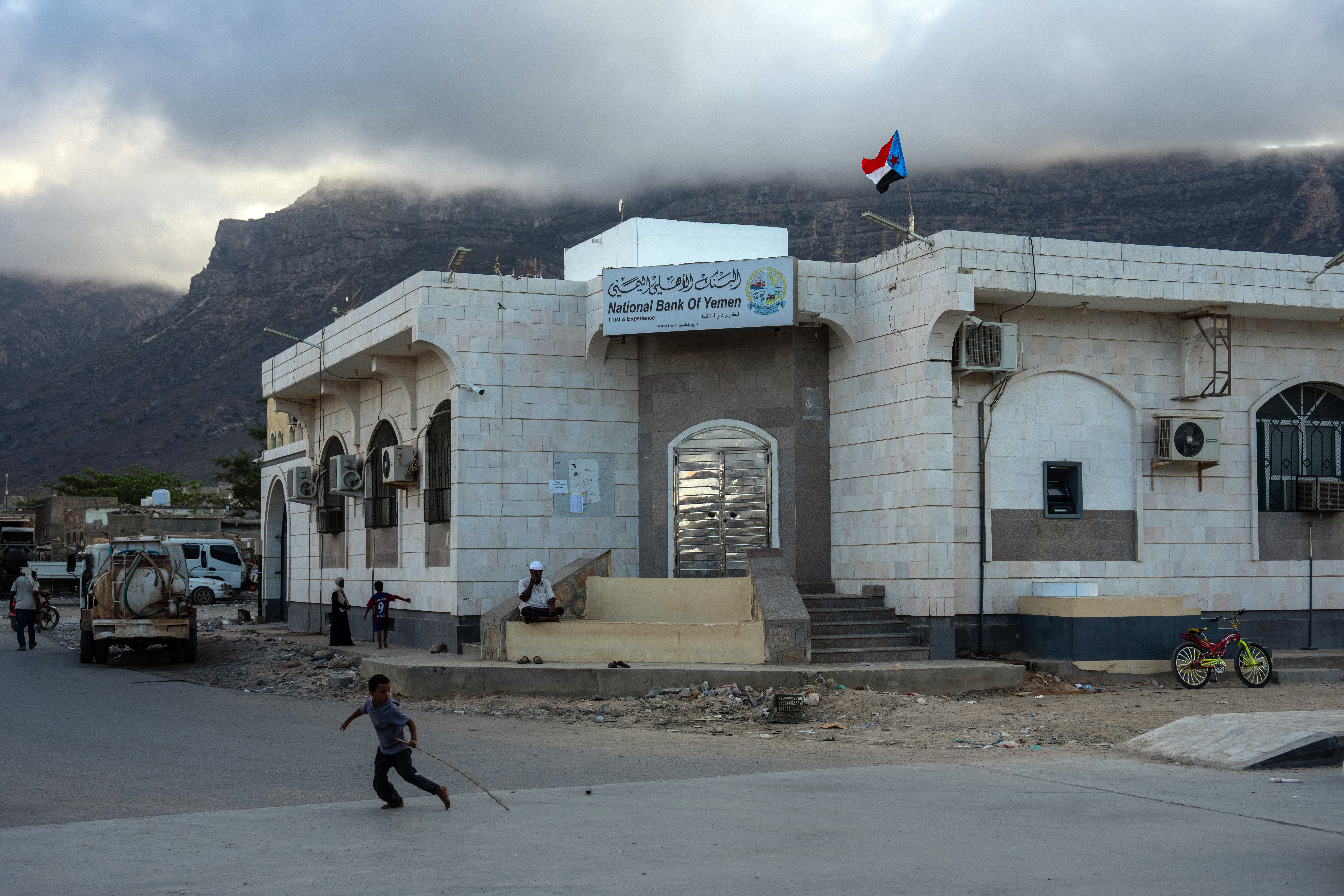 SOCOTRA ISLAND, YEMEN - OCTOBER 16: A boy runs past a branch of the National bank of Yemen in the main town of Hadibu on October 16, 2025 in Socotra, Yemen. Socotra, the largest island in an eponymous archipelago, lies 150 miles off the Horn of Africa, and even farther from mainland Yemen. Its relative isolation has mitigated the impact of Yemen's long-running and stalemated civil war, rendering it safe enough to attract a small but steady stream of foreign tourists. However, it has not been untouched by regional hostilities. In recent years, the UAE-backed secessionist group Southern Transitional Council wrested control of the island from the Saudi-backed internationally recognized government. The STC ultimately joined the government's Presidential Leadership Council, but the UAE retains considerable military and economic influence in the archipelago. (Photo by Carl Court/Getty Images)