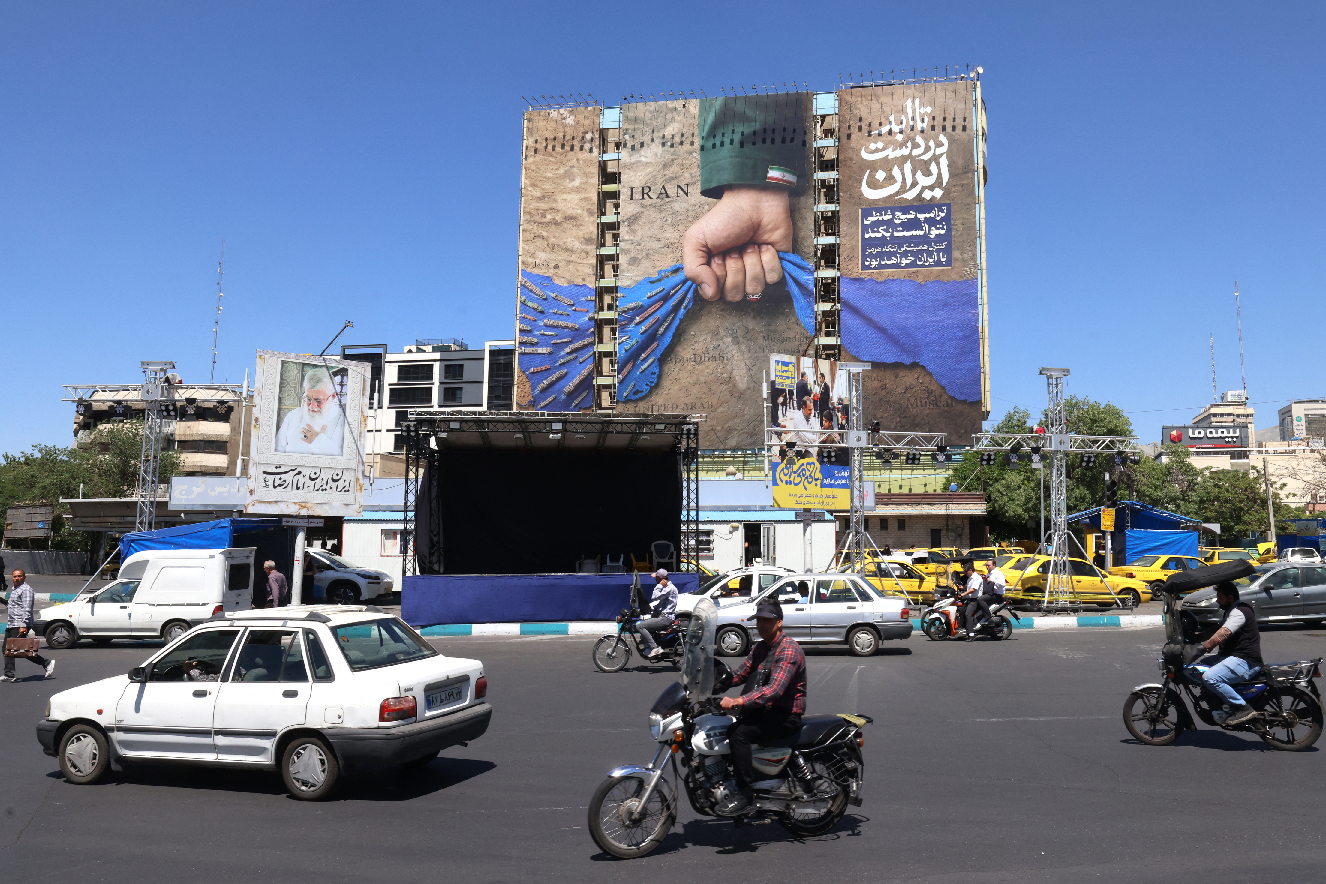 Vehicles drive past a billboard on the facade of a building depicting the Strait of Hormuz