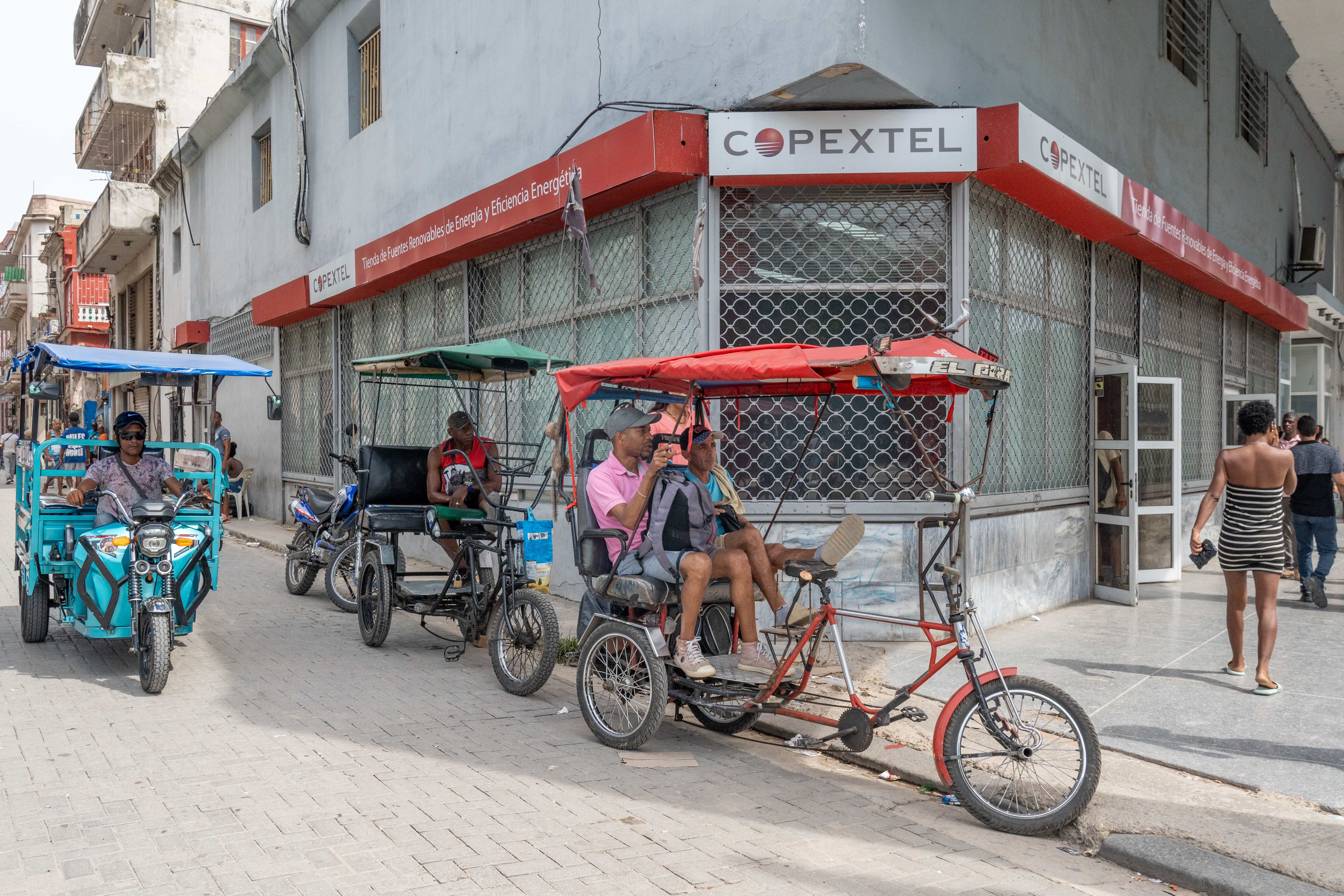 Pedicabs and an electric tricycle pass a Copextel solar energy store in Centro Habana. [Al Jazeera]