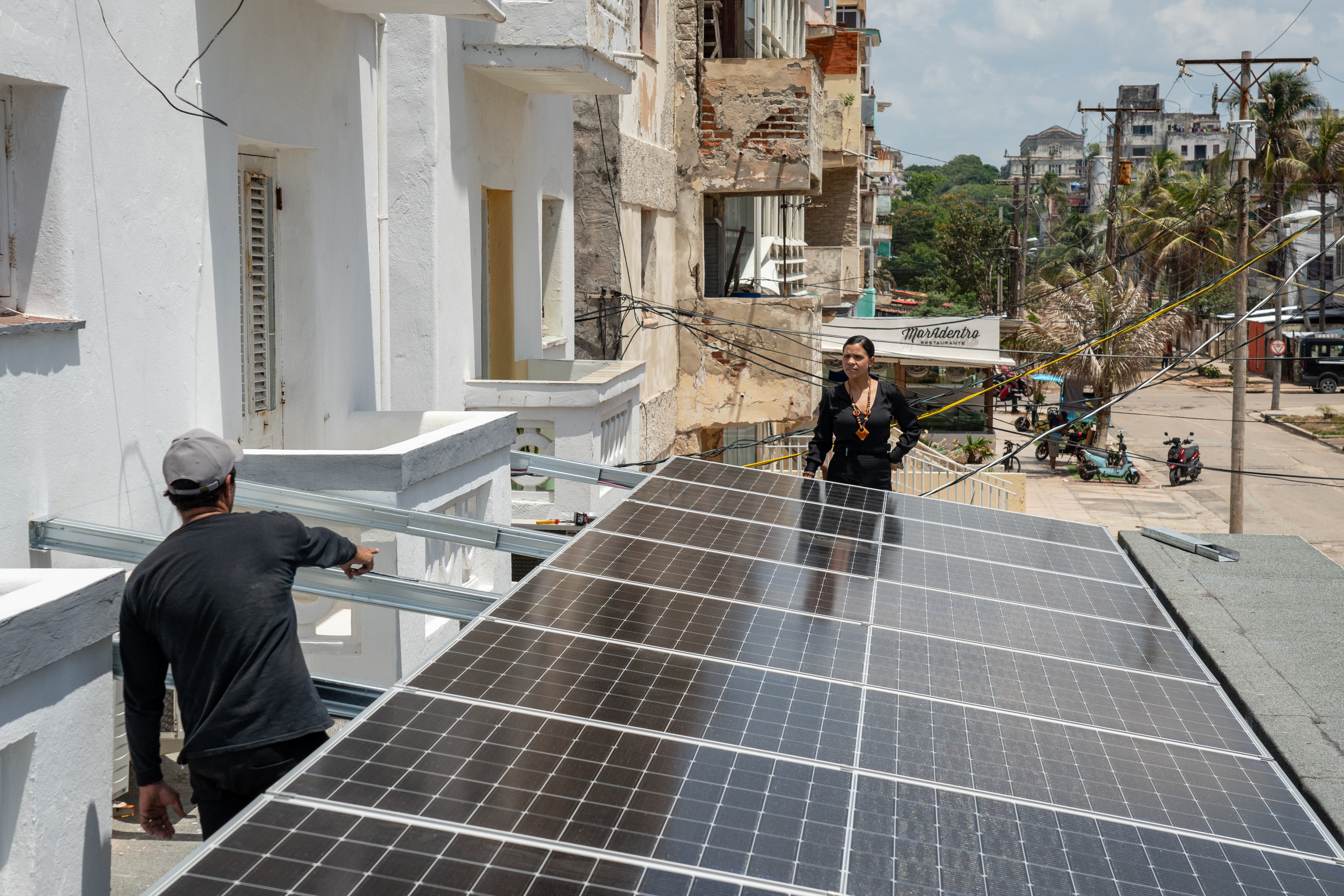 Aris Lopez Torres, owner of the Fuego Lento restaurant, speaks with technician Josecal Duarte during the installation of solar panels on the roof of her business along Havana’s Malecón.