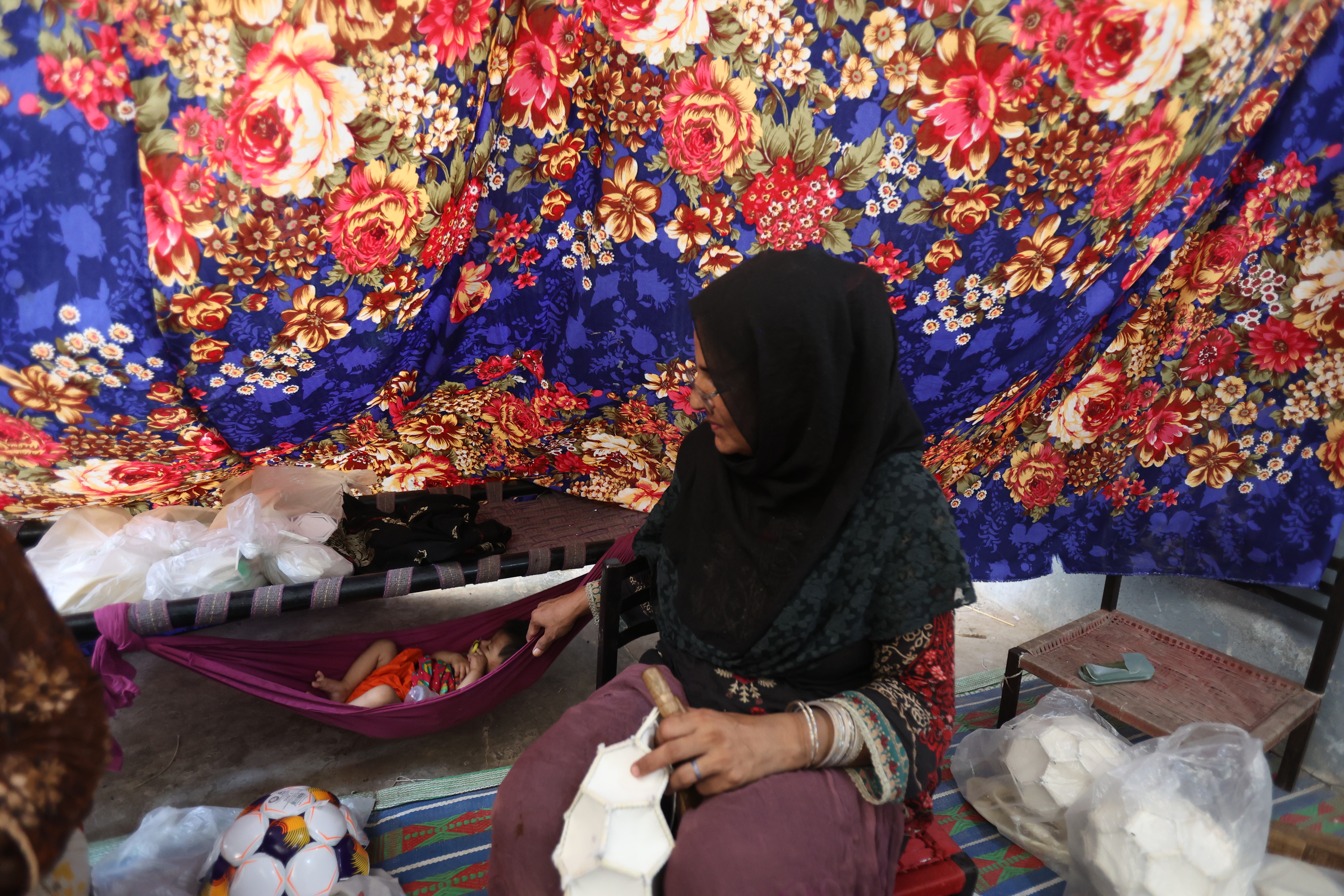 A mother gently rocks her baby in a makeshift cradle while working