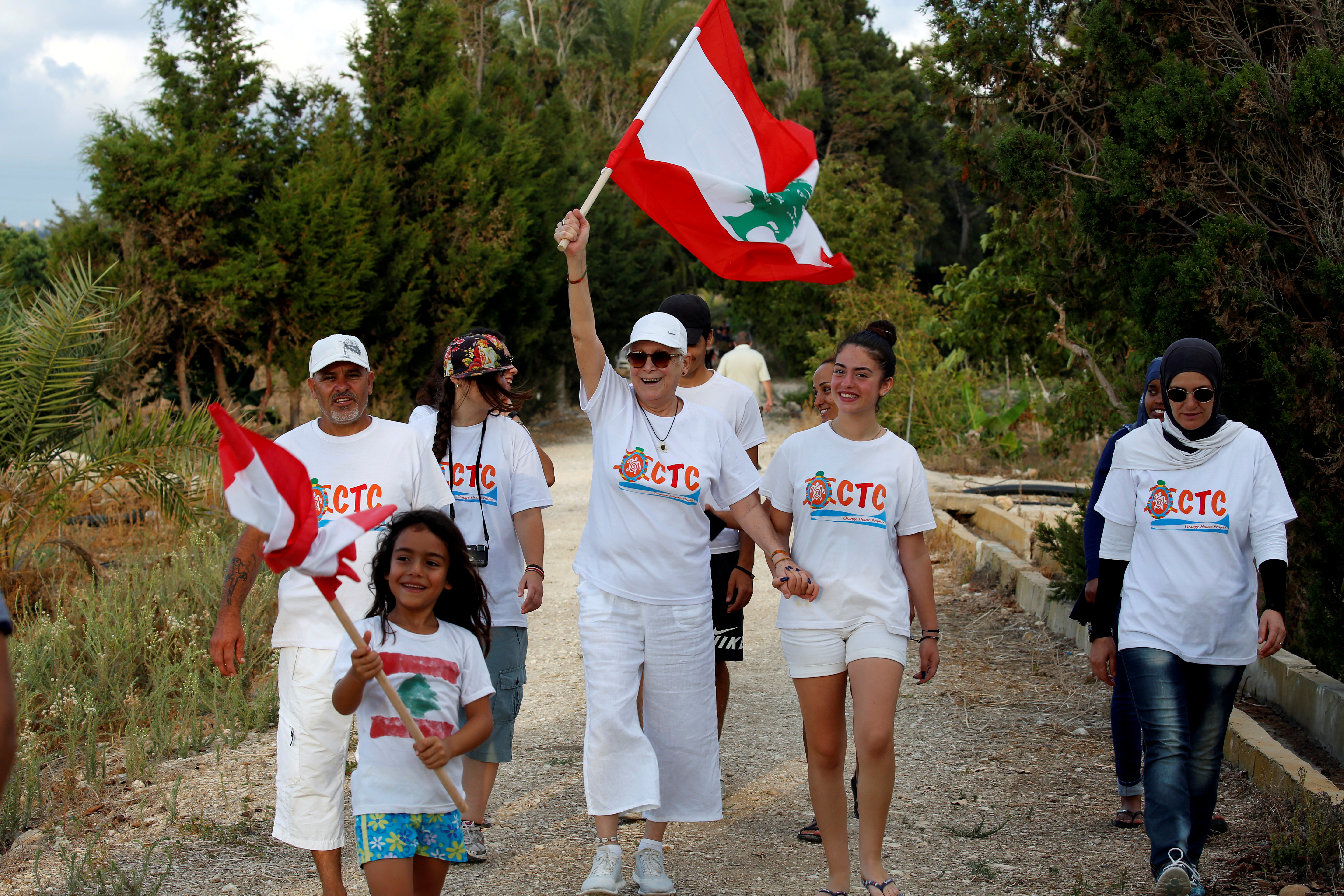 Mona Khalil holds a Lebanese flag as she walks with a group of people.