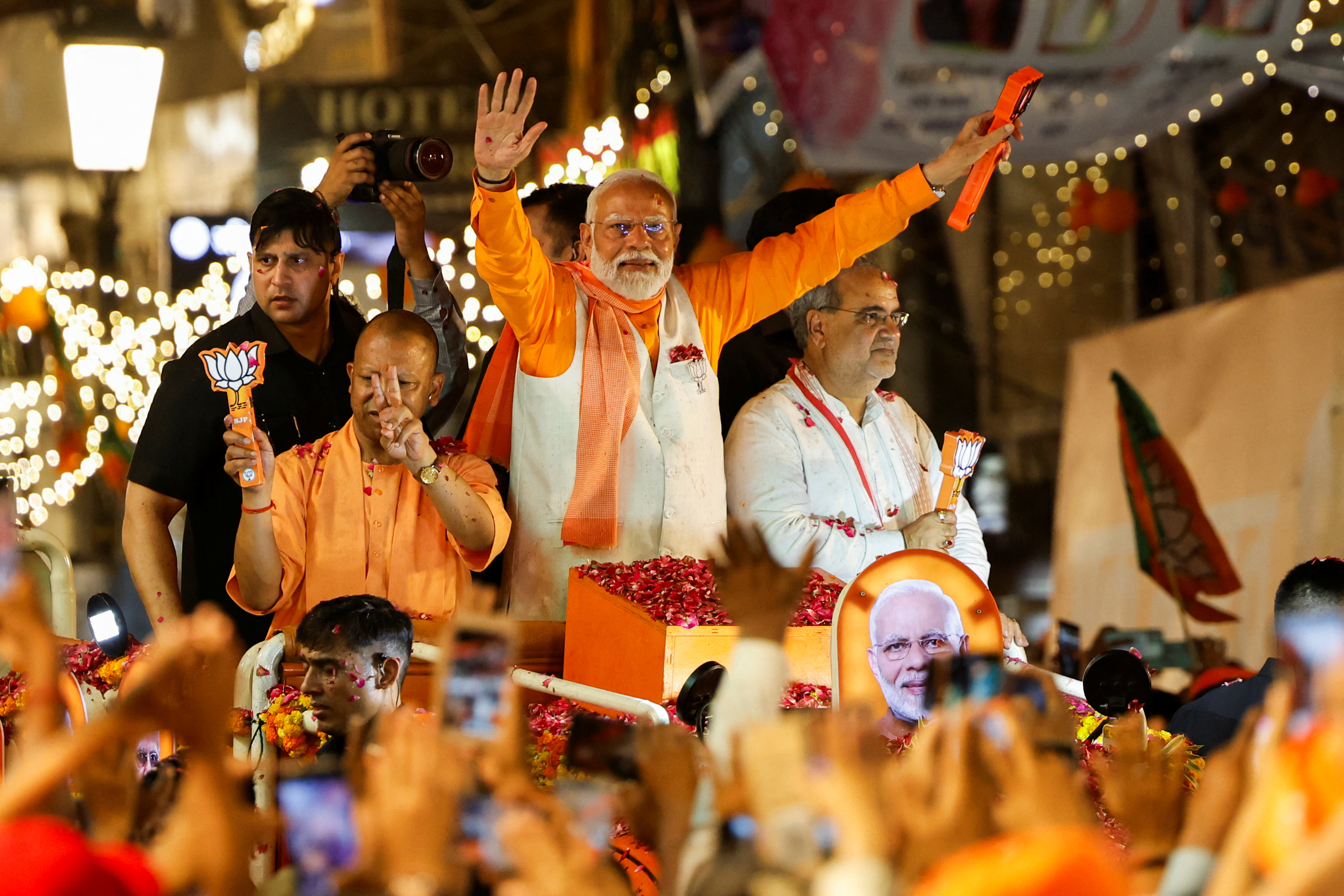 Indian Prime Minister Narendra Modi (with his arms outstretched) and Uttar Pradesh Chief Minister Yogi Adityanath (just to the left of Modi) show the BJP symbol during a roadshow as part of an election campaign in Varanasi, India, on May 13, 2024