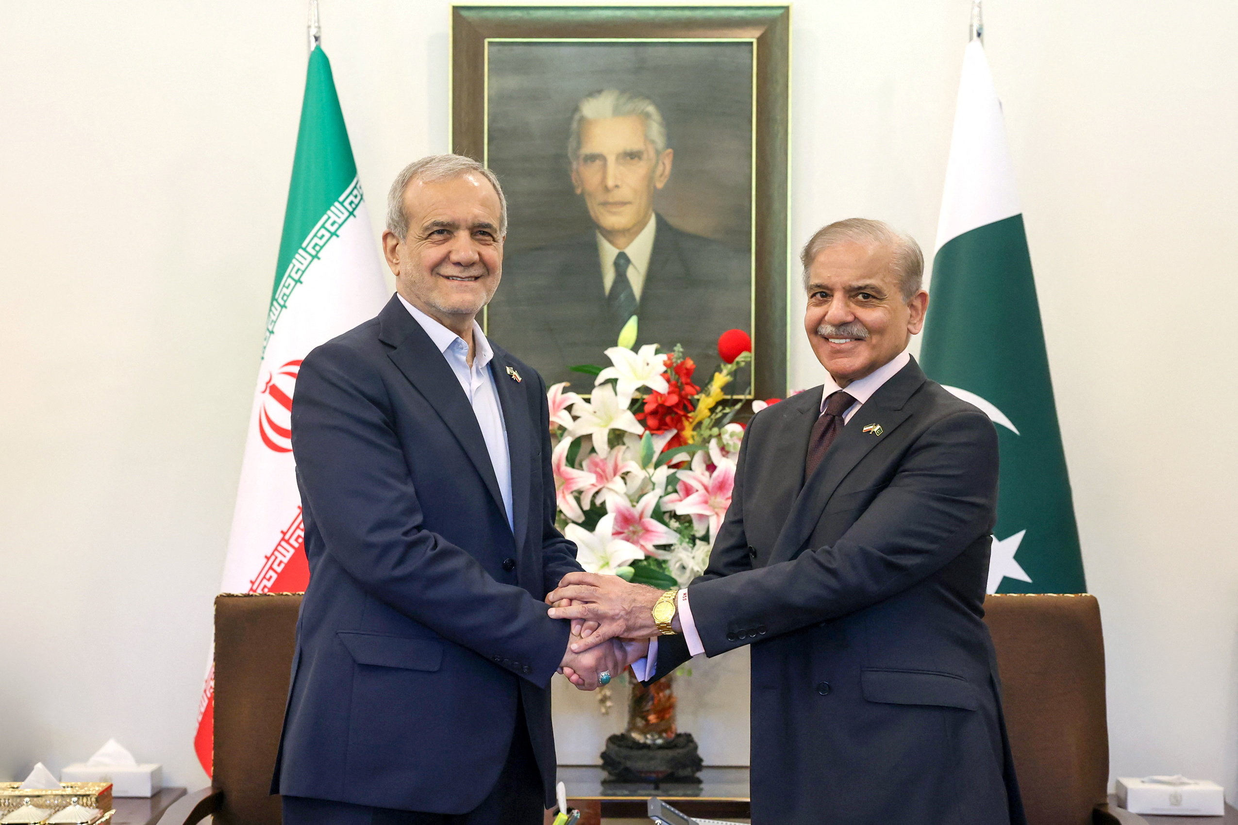 Iranian President Masoud Pezeshkian shakes hands with Pakistani Prime Minister Shehbaz Sharif as they smile for a photo.