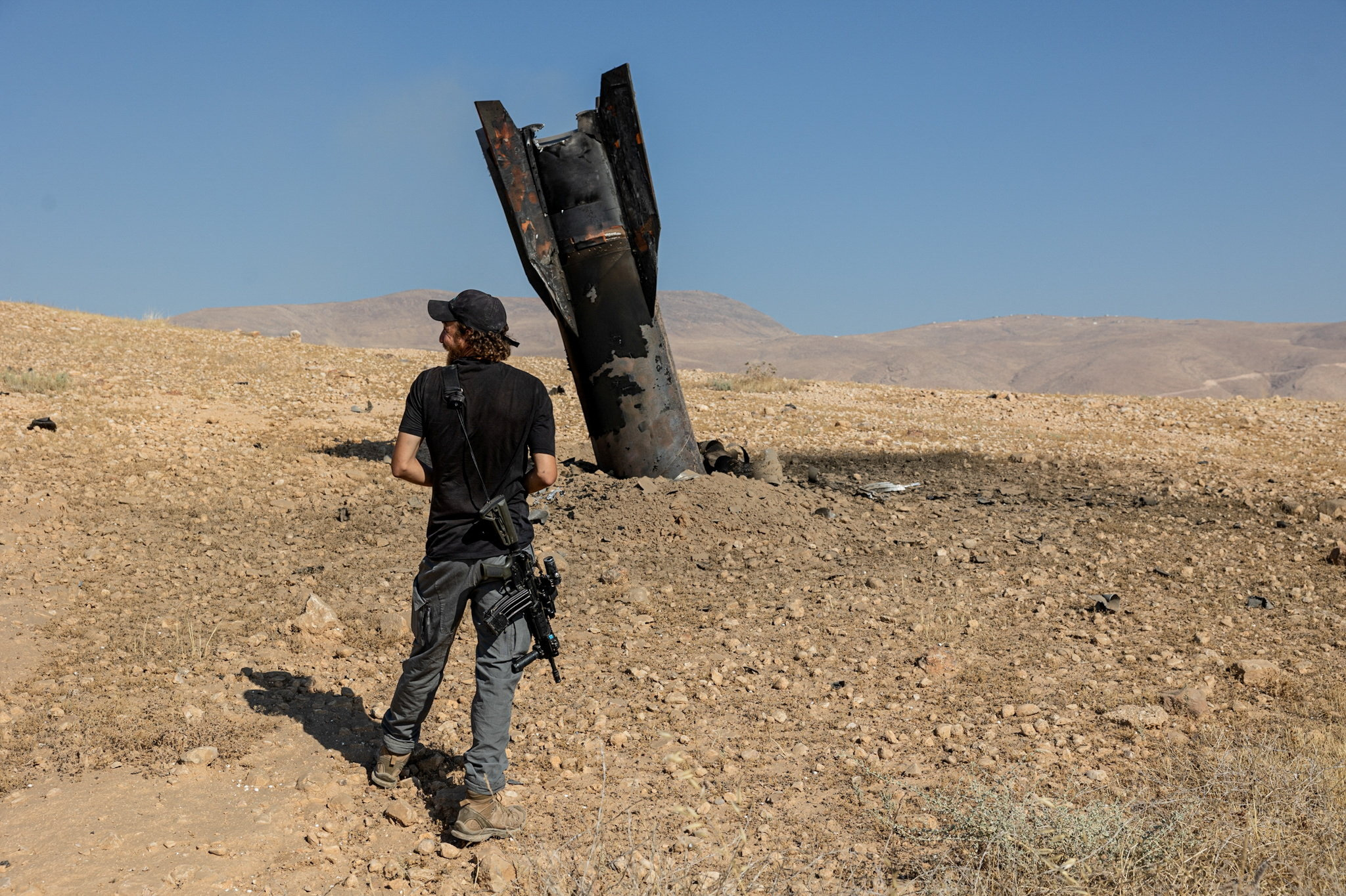 An Israeli settler stands next to part of a missile protruding from the ground.