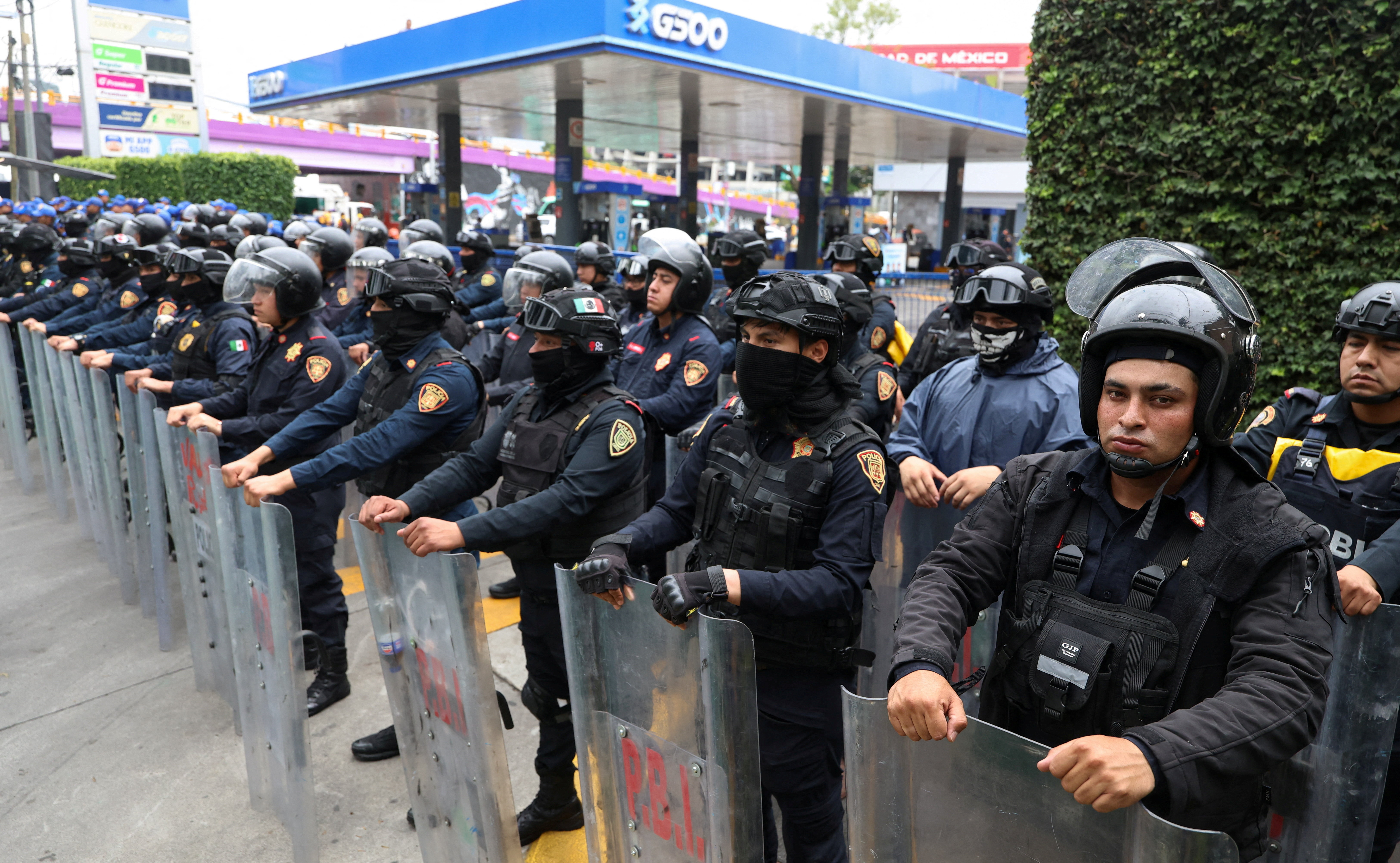 Police officers stand guard on a sidewalk with riot shields and helmets
