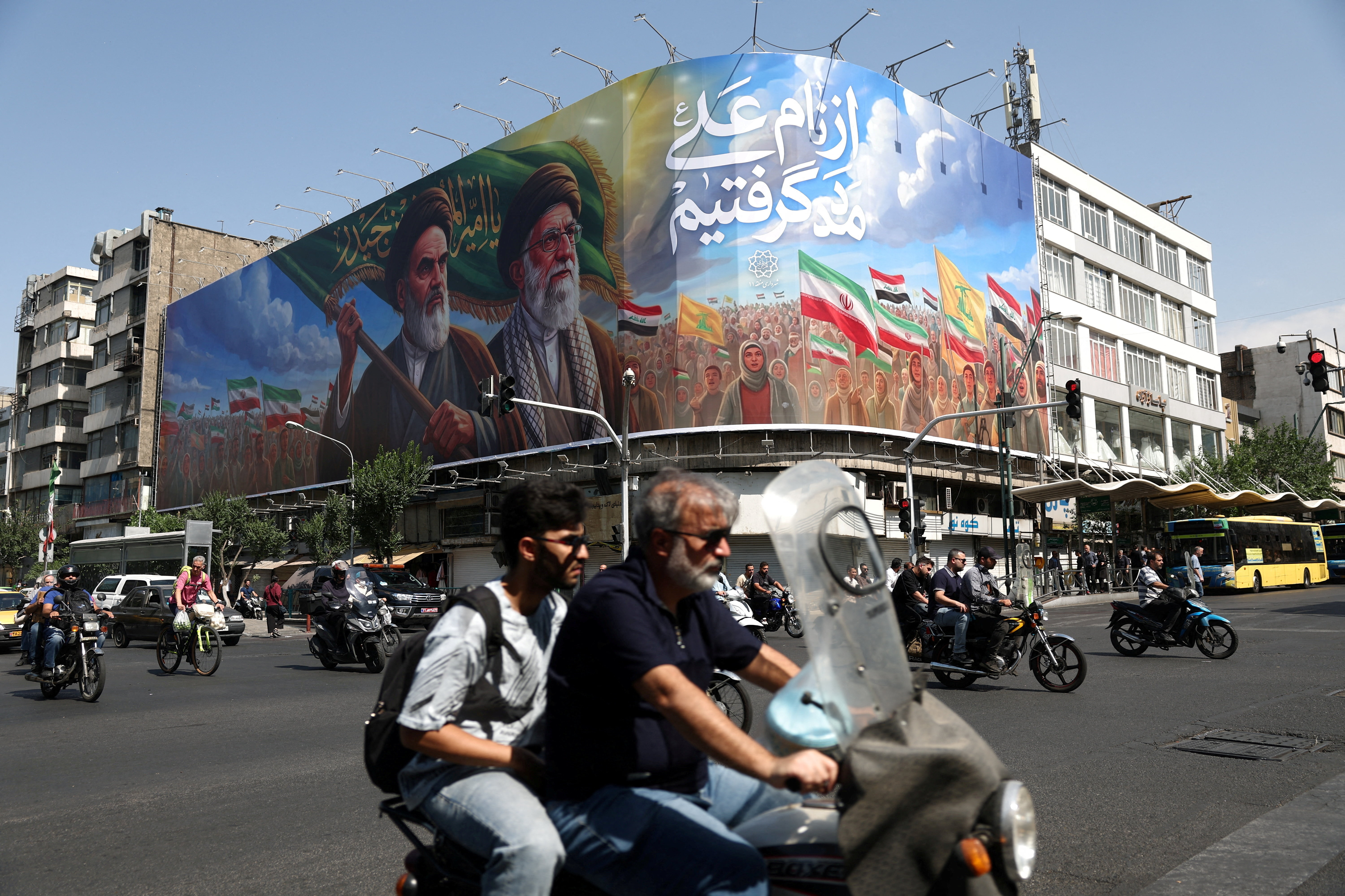 People ride past a billboard depicting the late leader of the Islamic Revolution, Ayatollah Ruhollah Khomeini, and the late Iran's Supreme Leader Ayatollah Ali Khamenei,