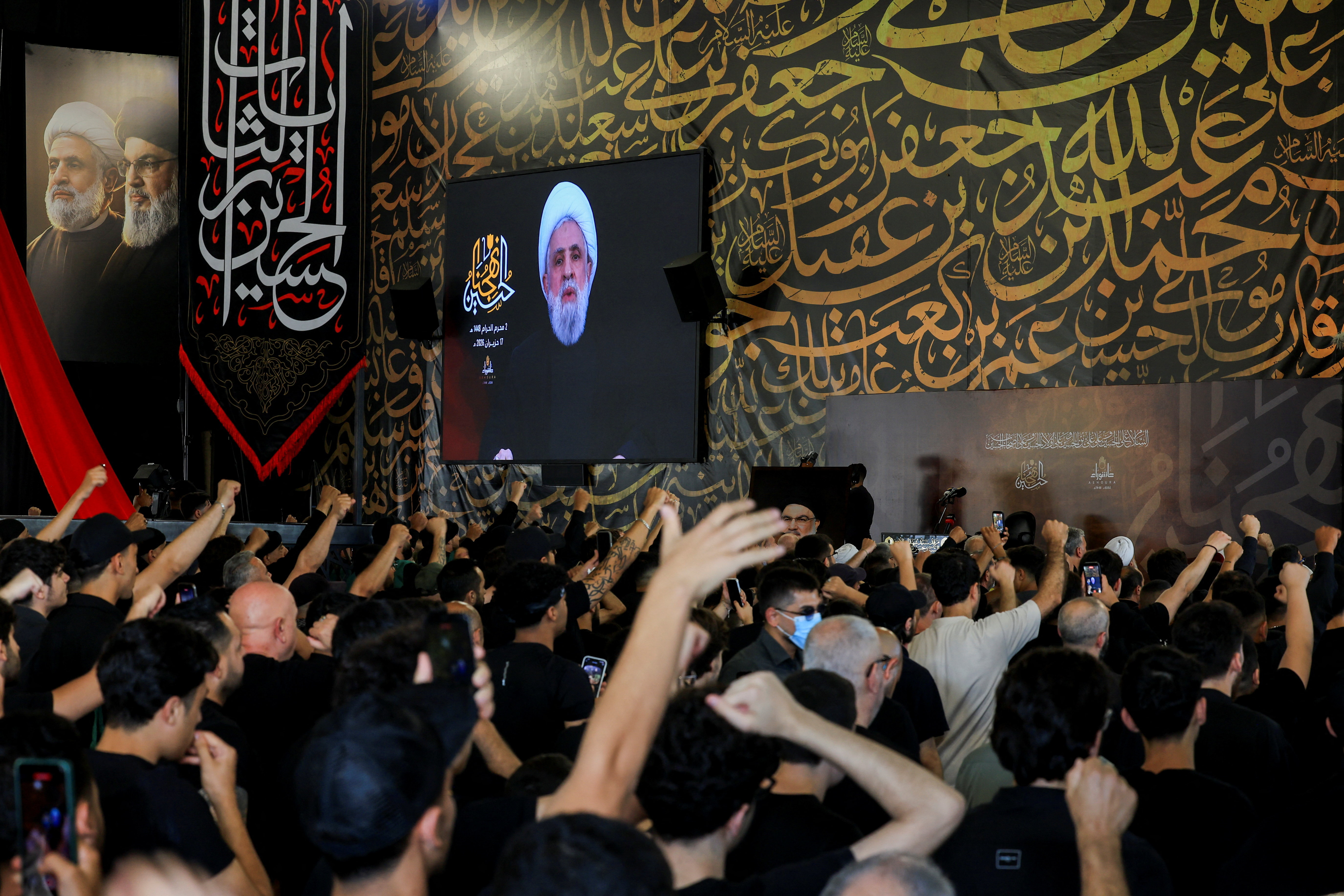 People react, as they watch Hezbollah chief Naim Qassem deliver a televised speech on a giant screen at the burial site of former Hezbollah leader Hassan Nasrallah, on the outskirts of Beirut, Lebanon, June 17, 2026