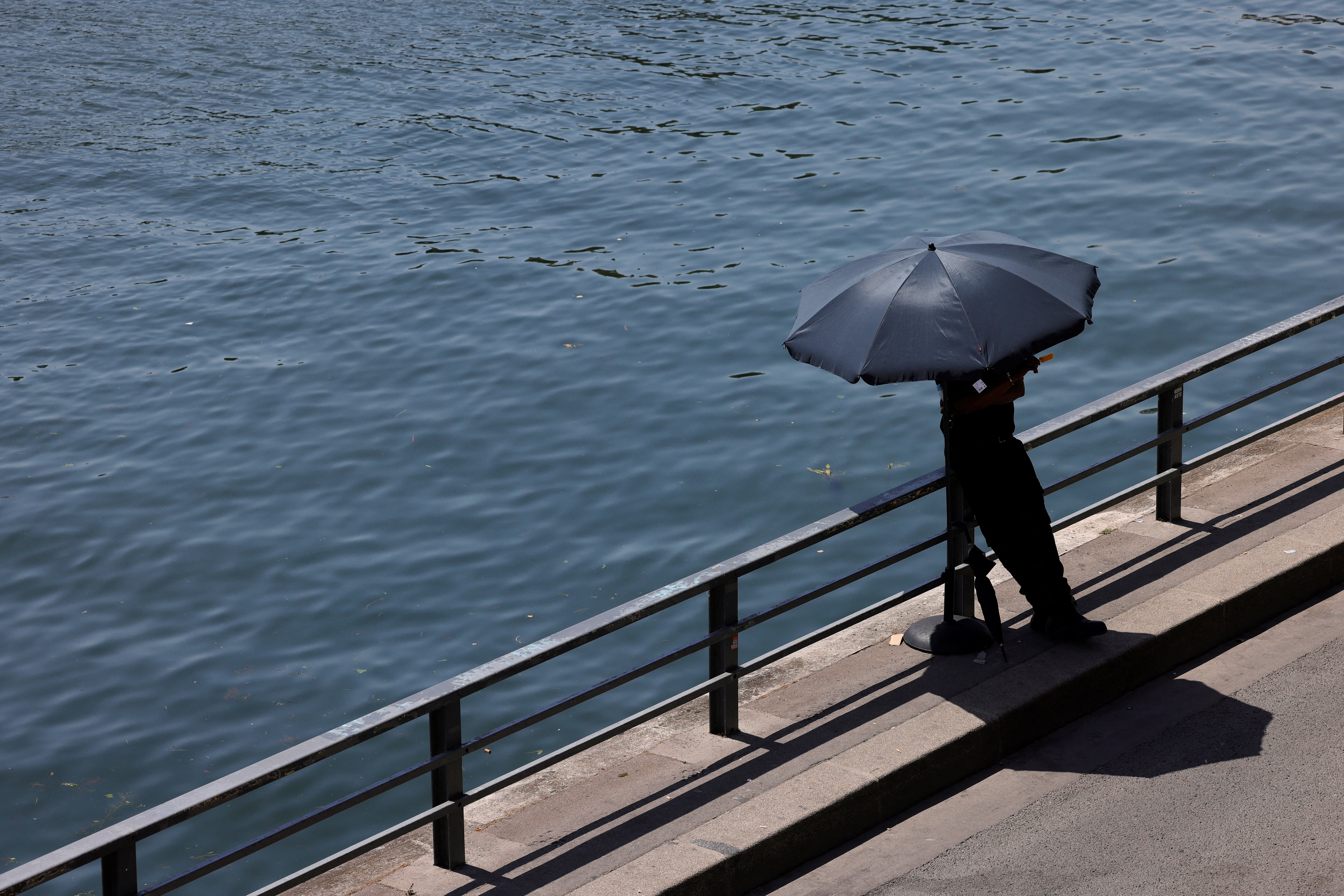 A person shelters from the sun under an umbrella along the banks of the River Seine in Paris as temperatures rise during a heatwave affecting a large part of France