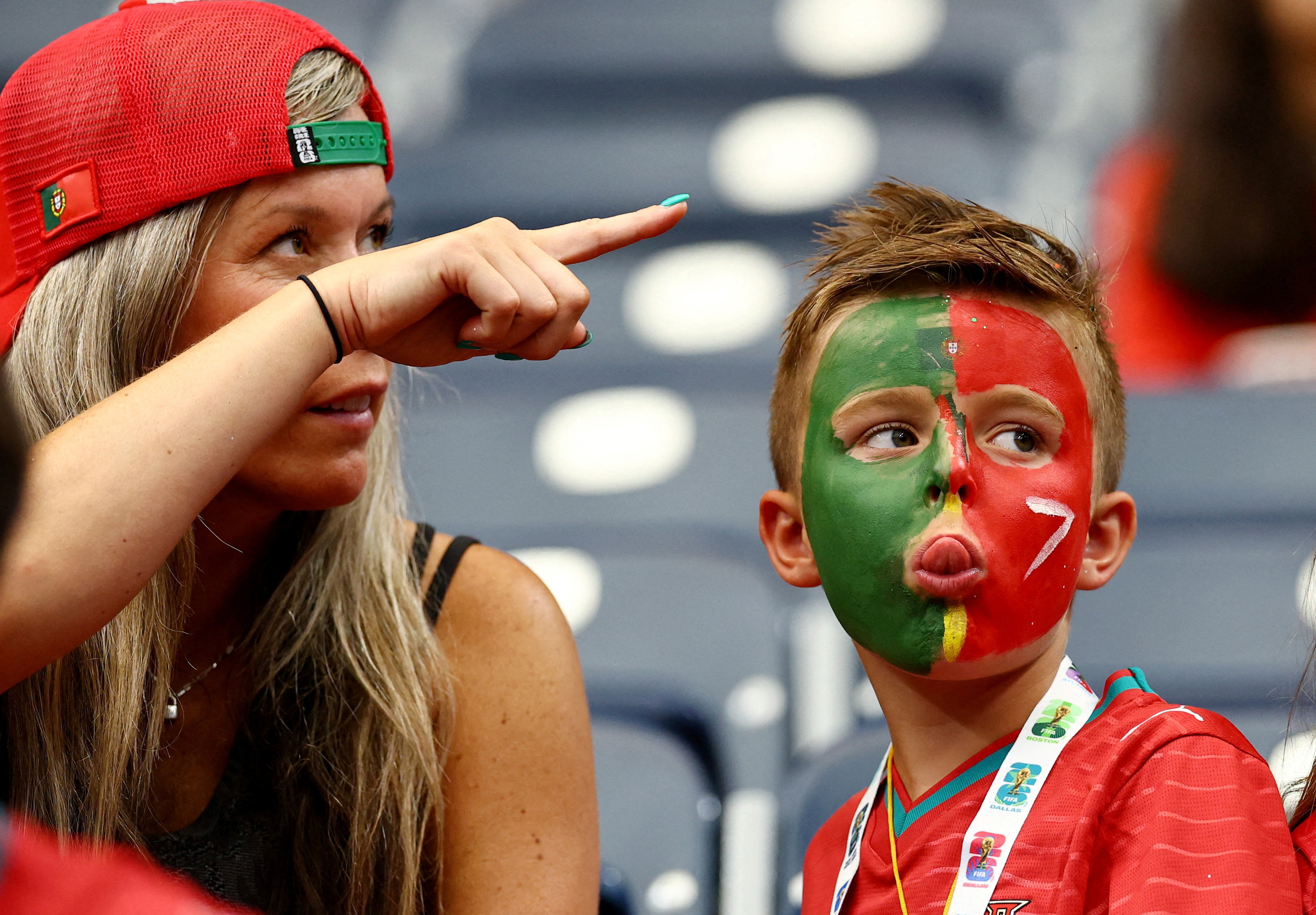 A woman points as she sits next to a child with his face coloured in the Portuguese flag.