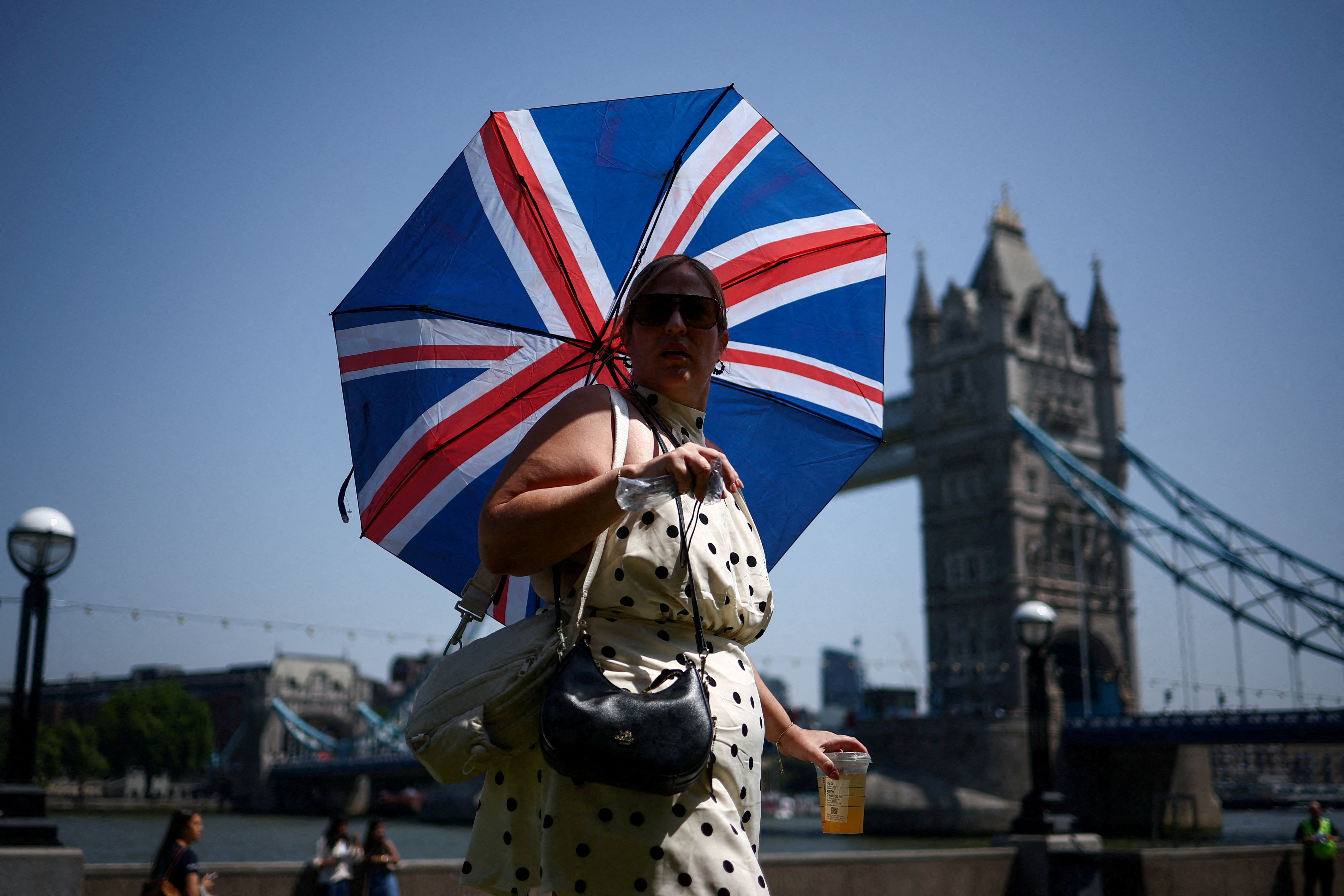 A woman uses an umbrella to shield herself from the sun while walking near Tower Bridge, amid a heatwave, as Britain experiences record temperatures disrupting schools and transport networks, in London, Britain, June 25, 2026. REUTERS/Guglielmo Mangiapane TPX IMAGES OF THE DAY
